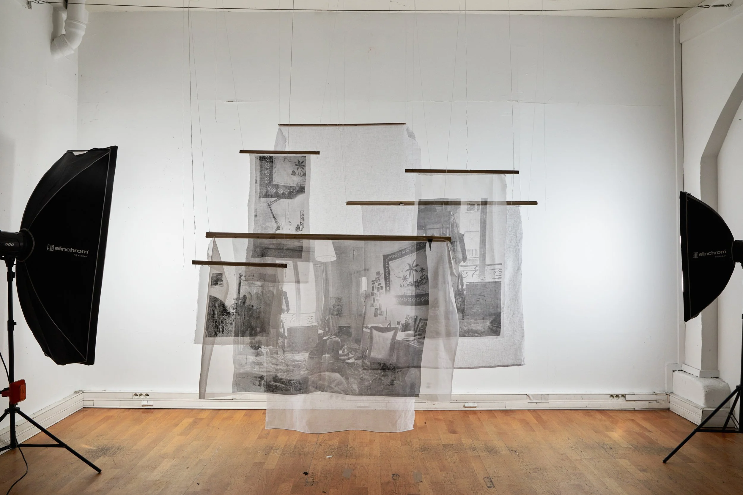 Installation artistique avec des tissus translucides suspendus avec des barres en bois, en studio avec deux projecteurs. 