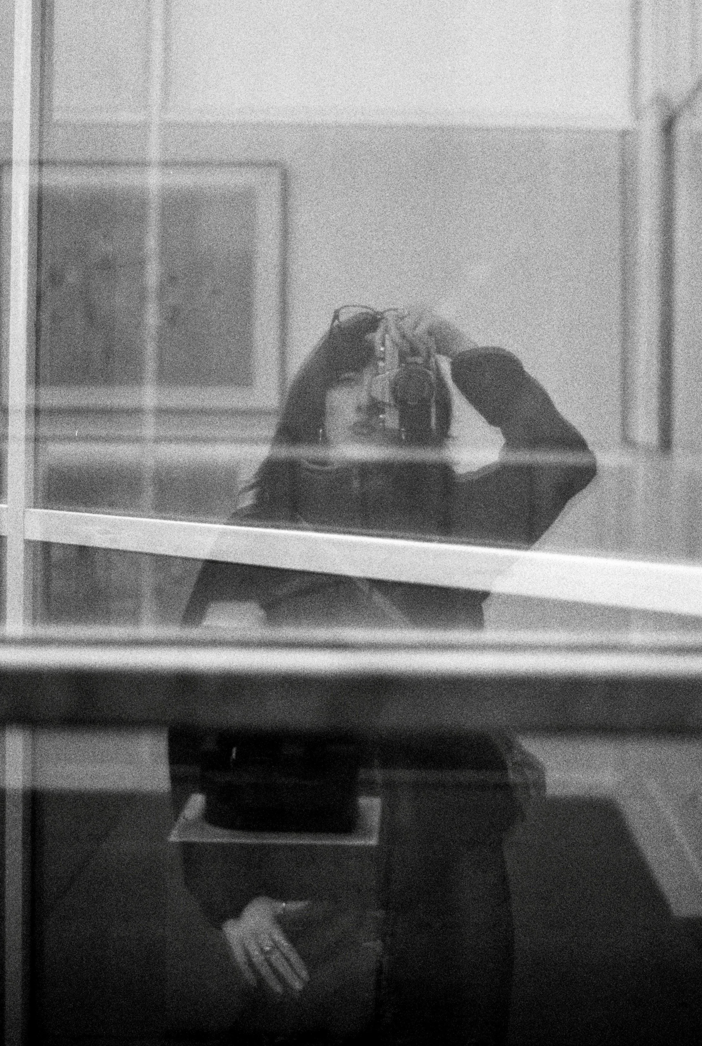 Reflet d'Enora Le Gall prenant une photo dans une vitre, en noir et blanc, dans un environnement exterieur