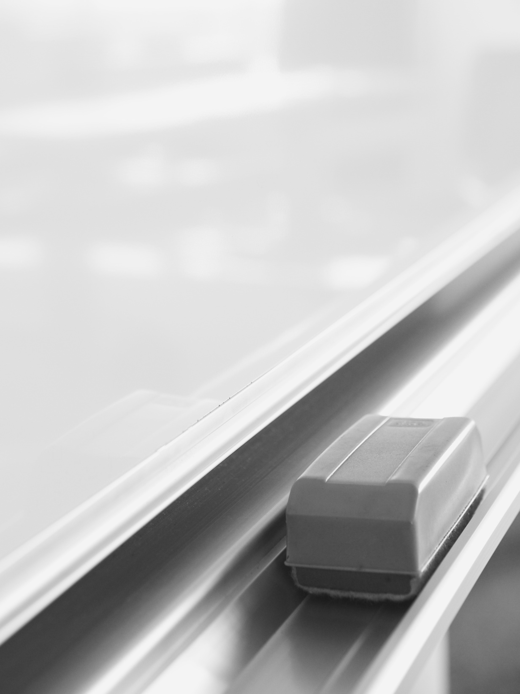 A close-up of a whiteboard eraser on a metal tray with a whiteboard in the background.