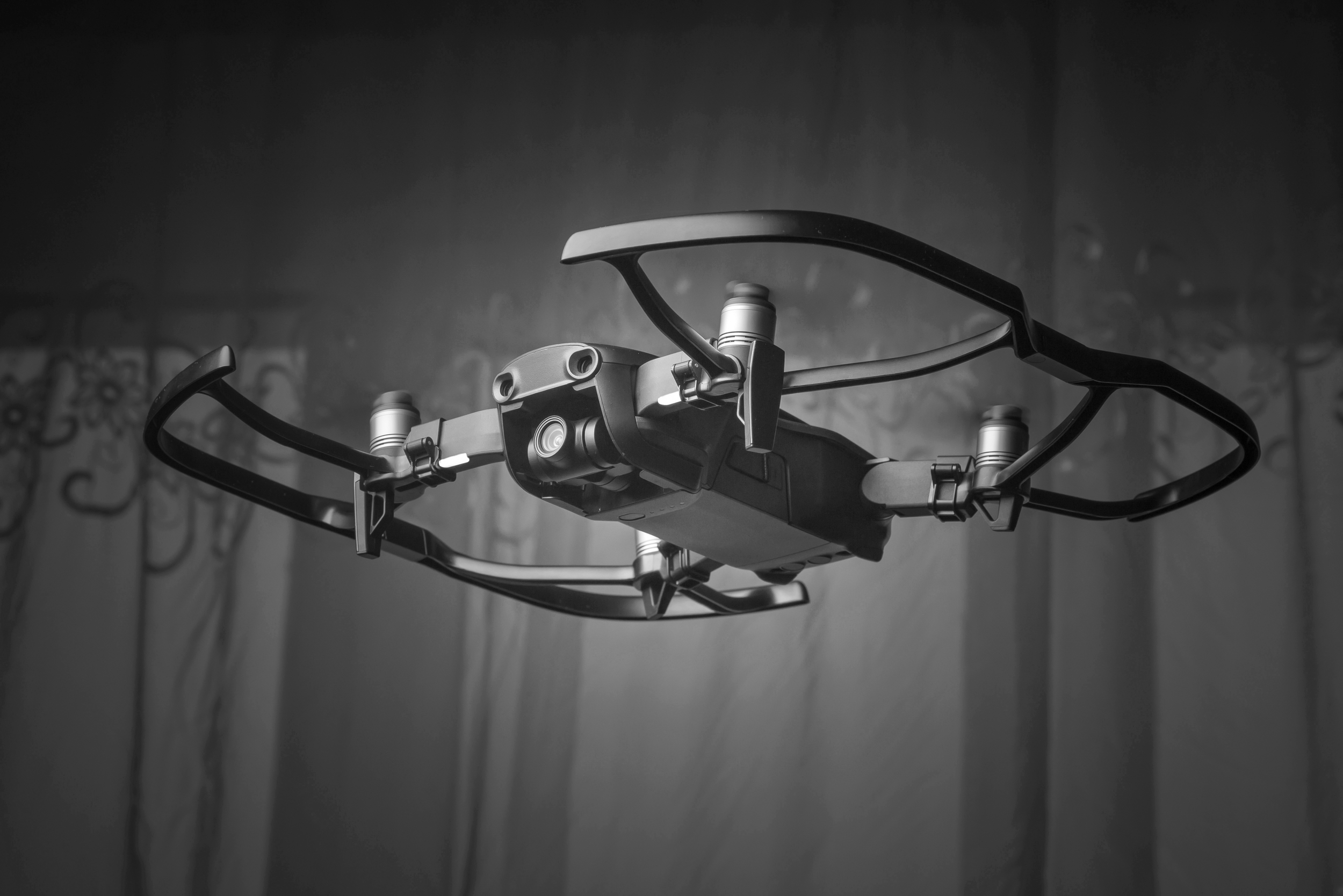 Black and white photo of a drone flying indoors against a wall.