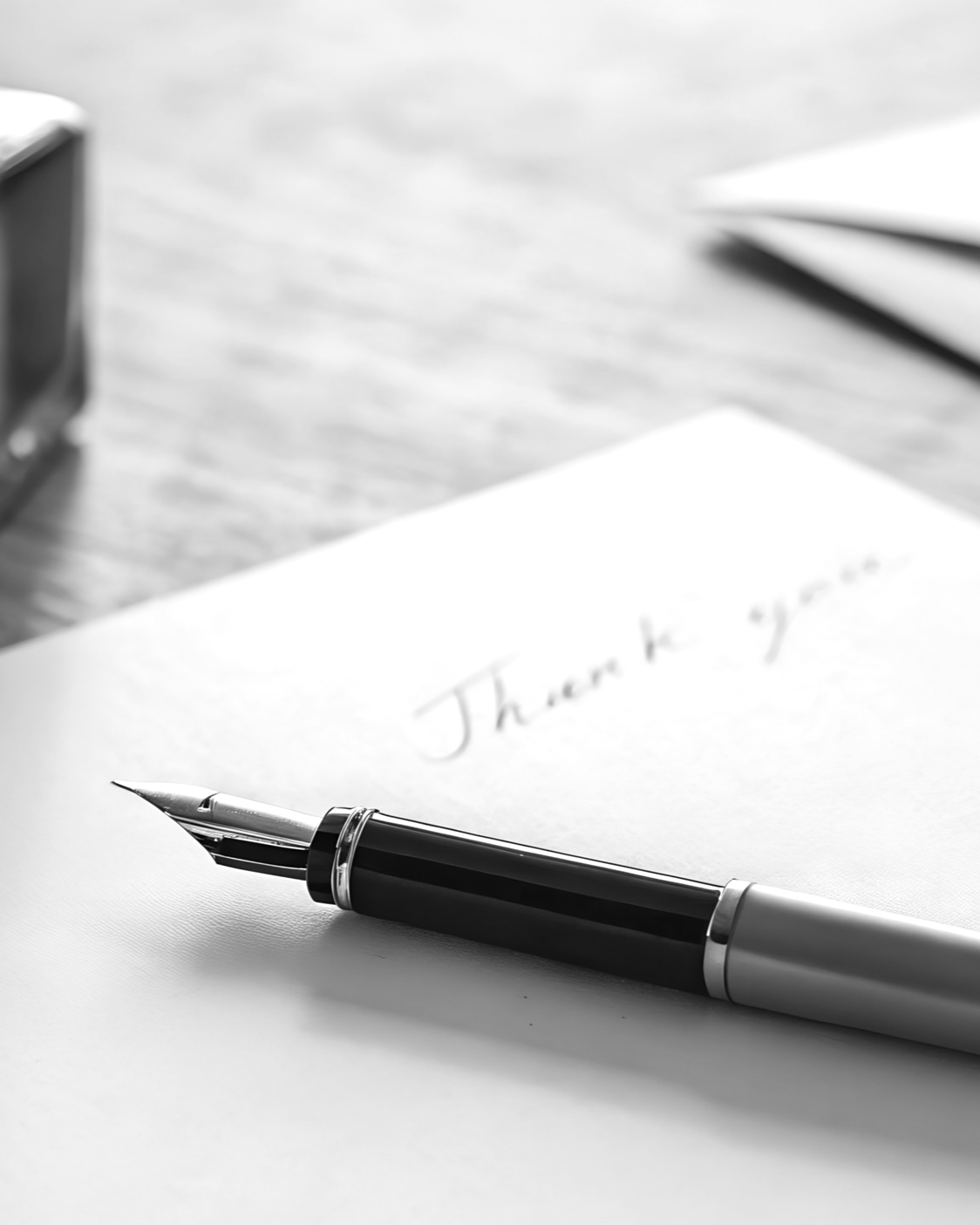 Close-up of a pen on a sheet of paper with 'Thank you' written on it, on a desk with other blurred objects in the background.