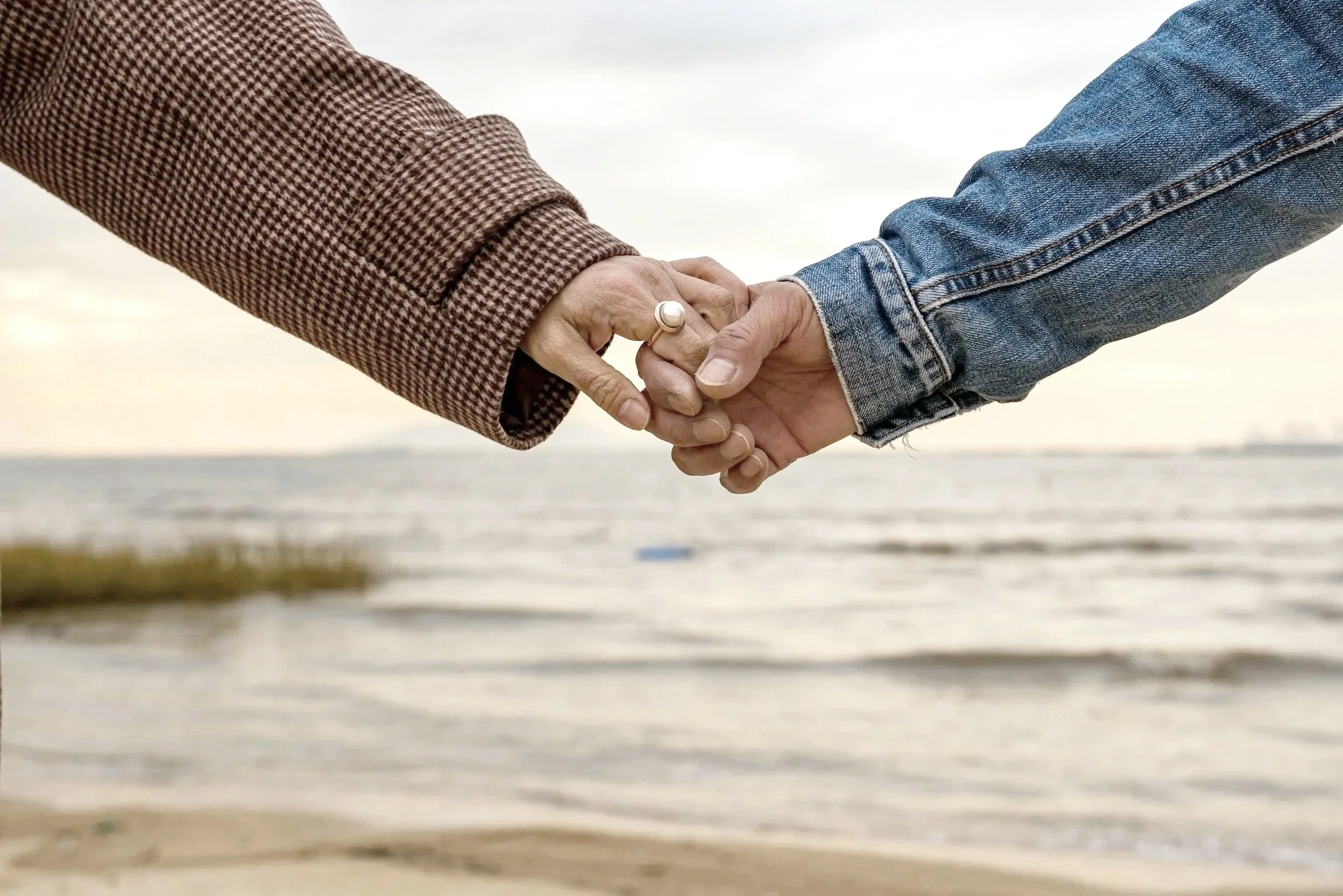Two people holding hands near a beach, with the ocean in the background.