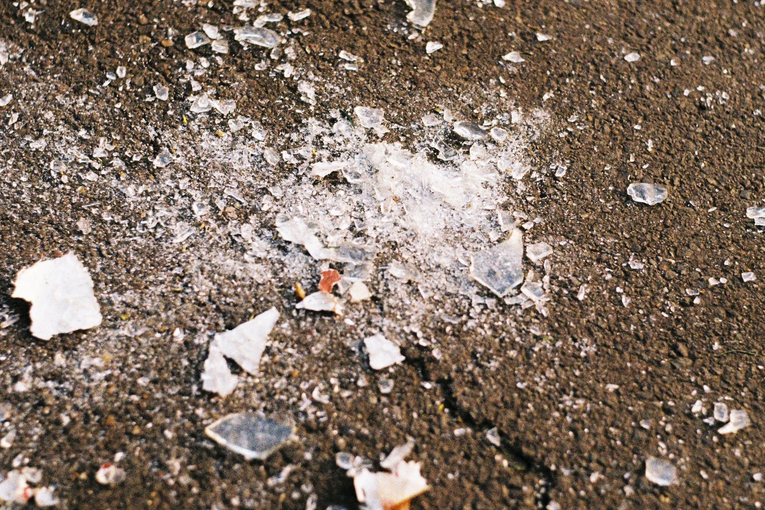 Restos de vidro quebrado espalhados sobre o chão de terra.