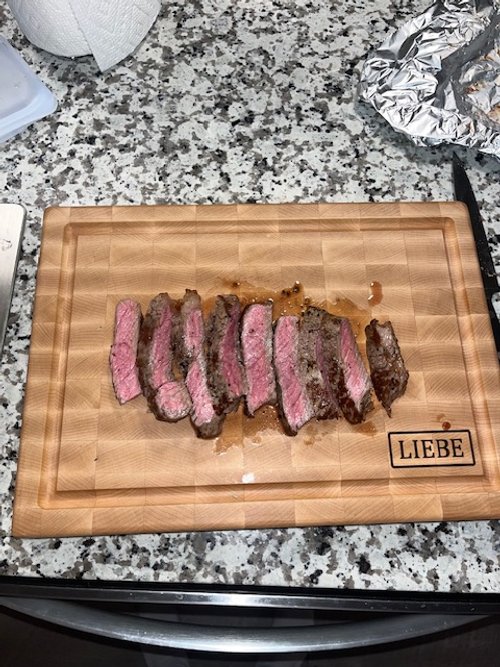 Sliced medium-rare steak on a wooden cutting board with the word "LIEBE" engraved in one corner, placed on a granite countertop.