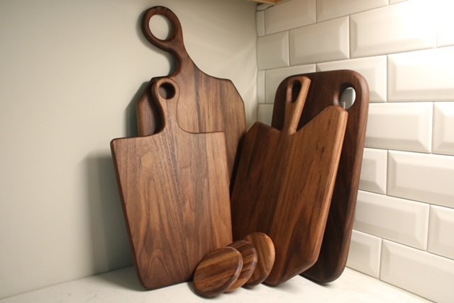 Set of wooden cutting boards and round wooden coasters on a kitchen countertop, with white subway tile backsplash.