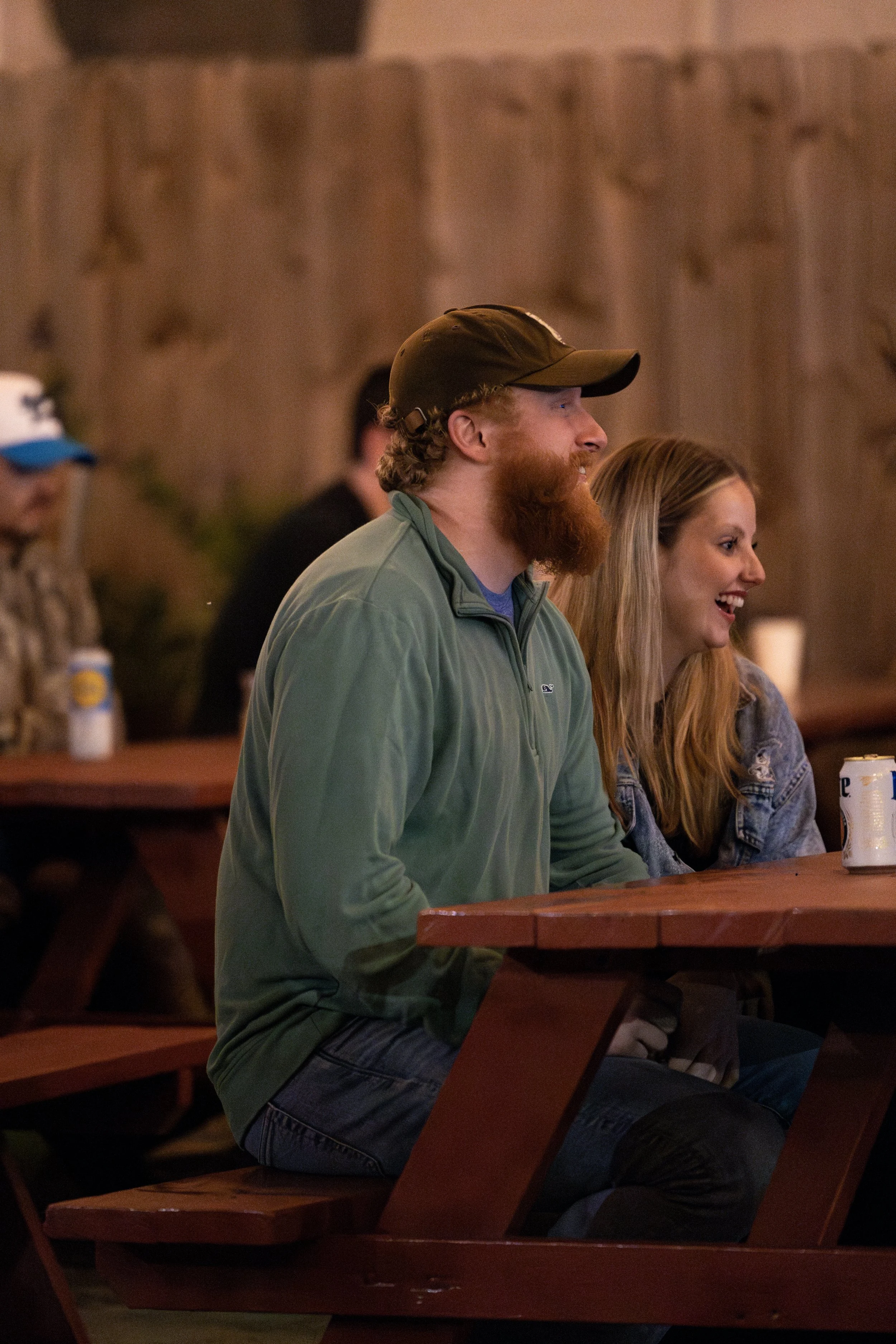 People sitting at a wooden table, smiling and enjoying themselves, with a rustic wooden wall in the background.