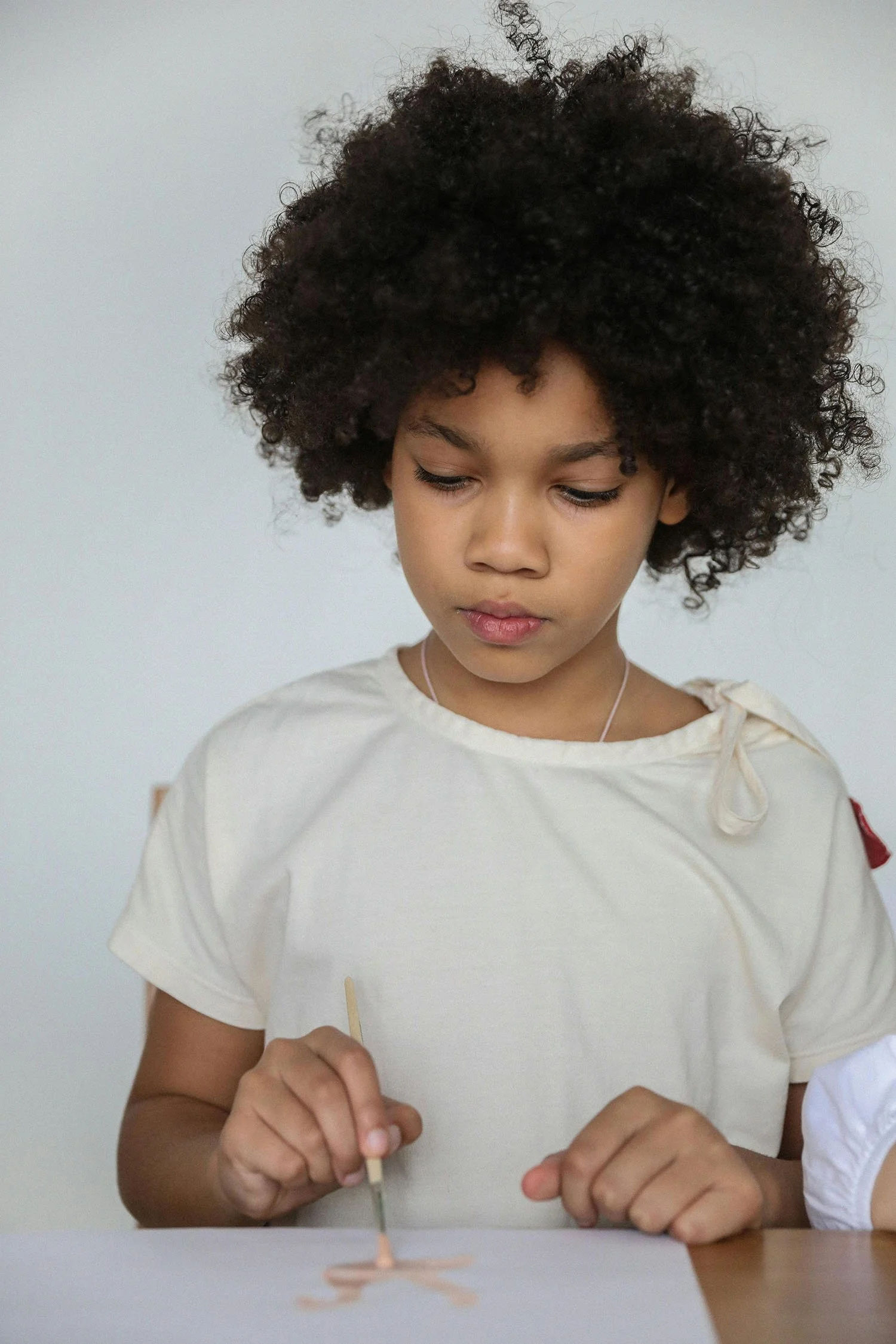 Child with curly hair painting with a small brush on a piece of paper.