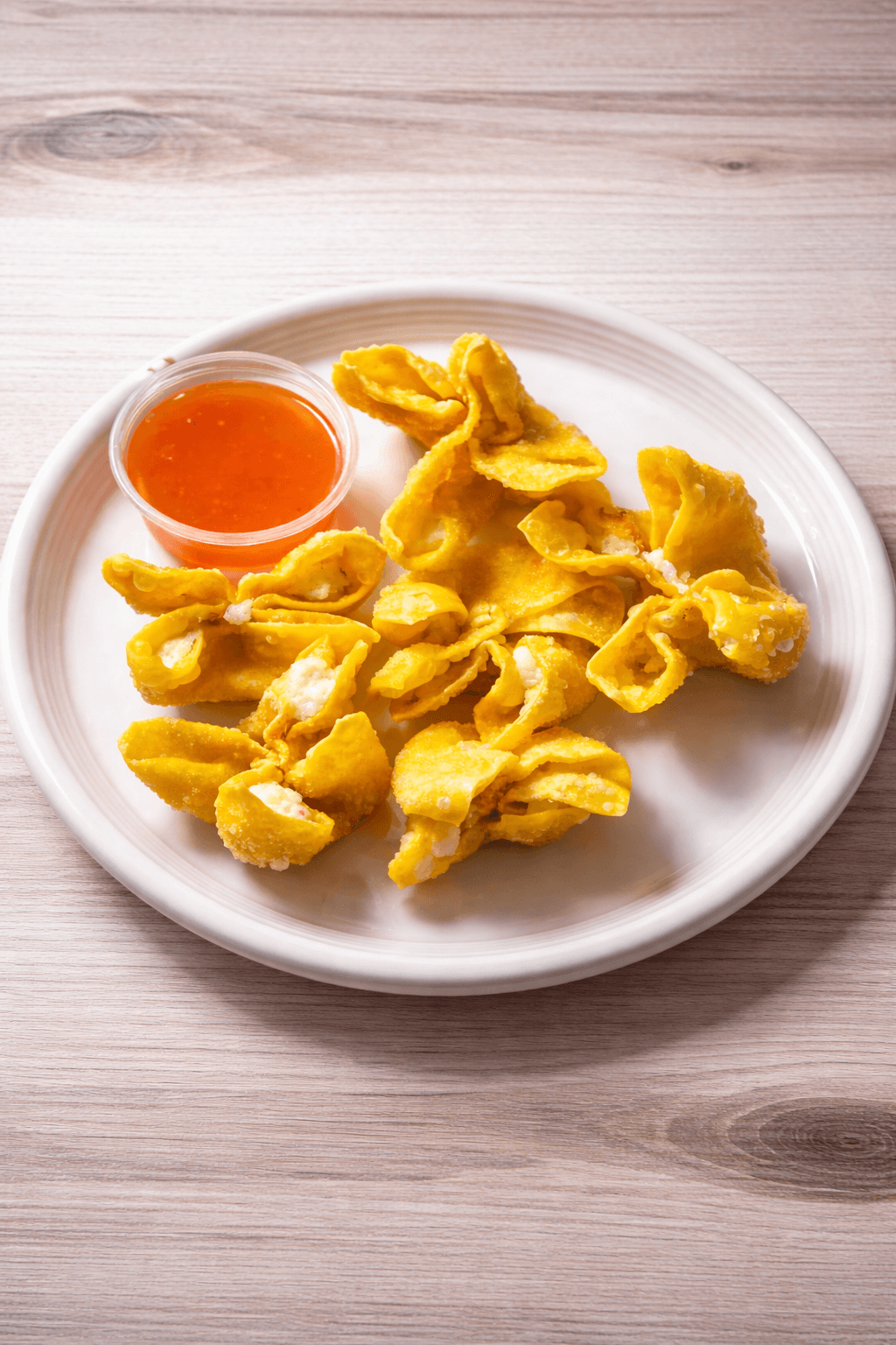 Fried wonton dumplings with a small cup of orange dipping sauce on a white plate.
