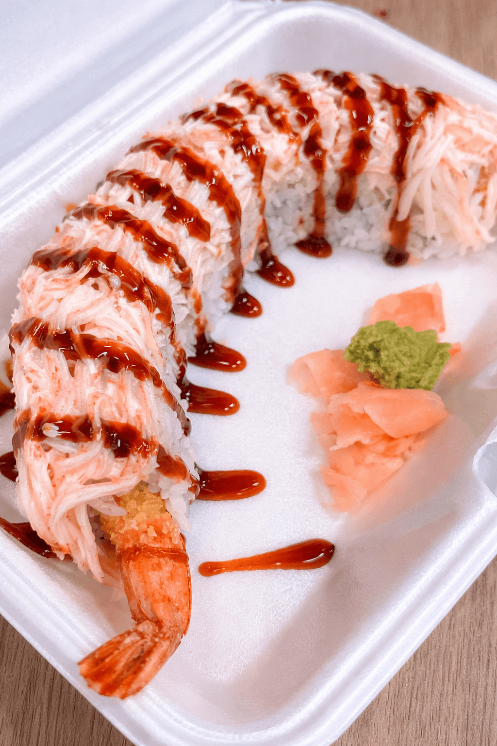 A sushi roll topped with shredded crab meat, drizzled with eel sauce, served with wasabi and pickled ginger.