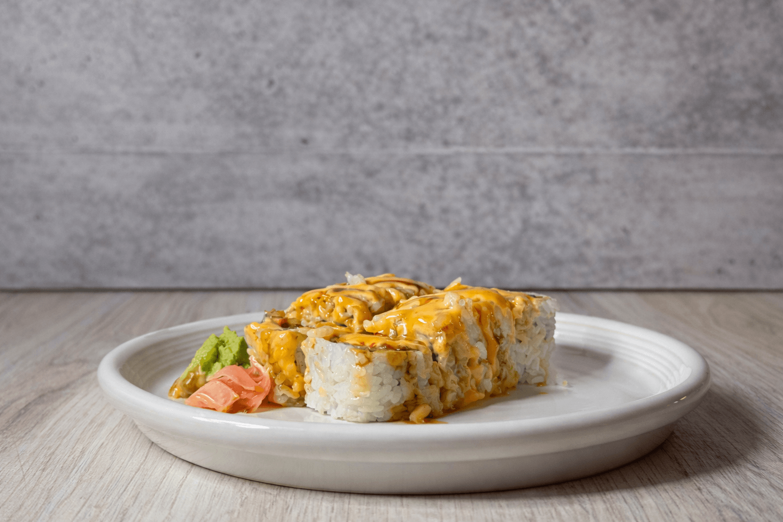 Sushi roll topped with sauce, served with pickled ginger and wasabi on a white plate