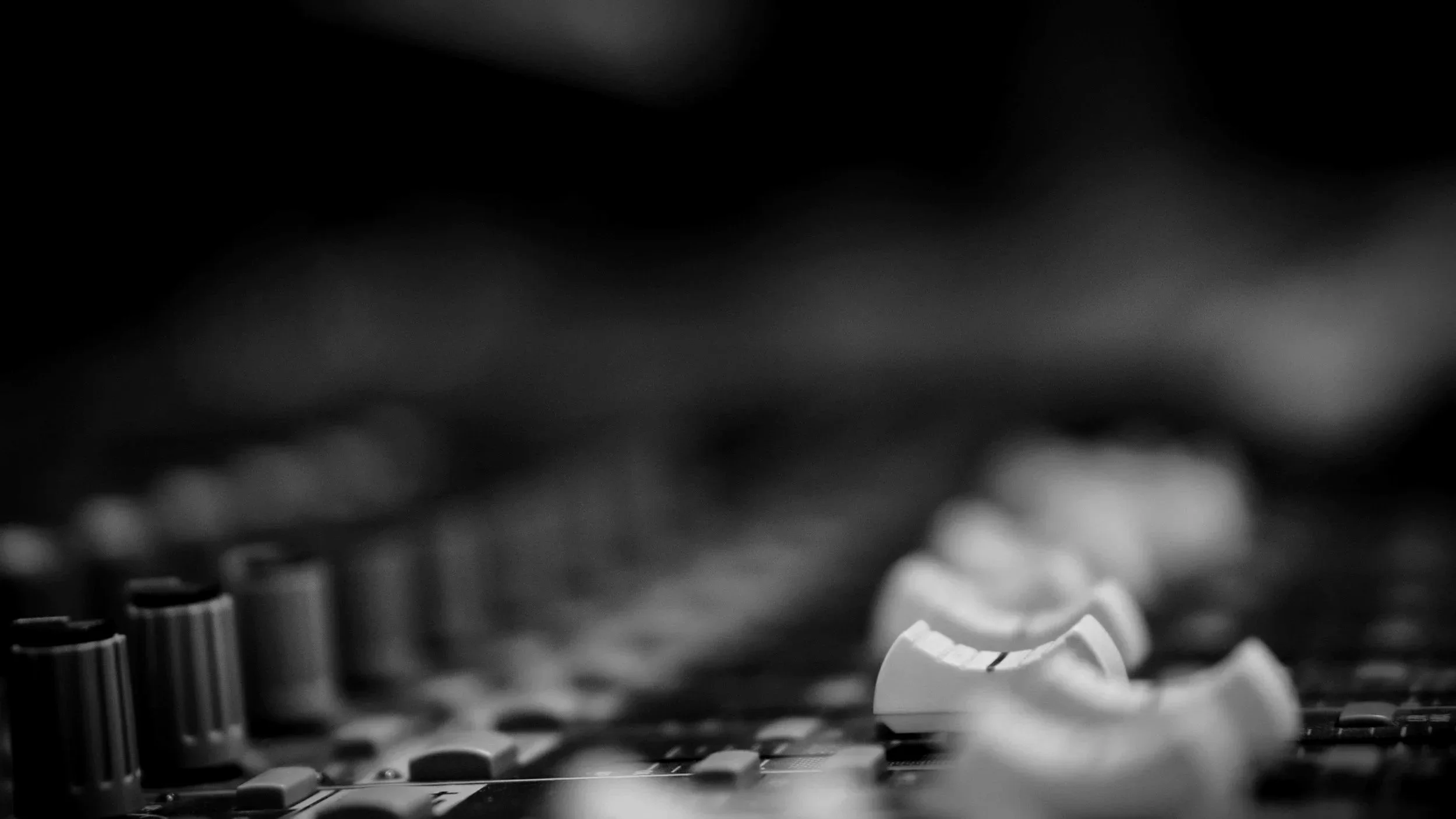 Close-up of an audio mixing console with knobs and sliders in black and white.