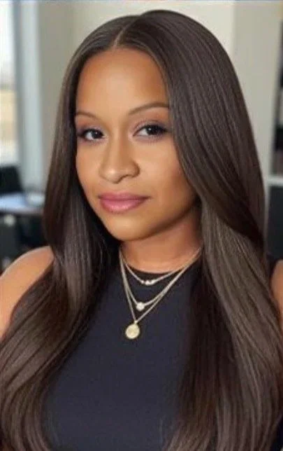 Young woman with long, straight hair, wearing a sleeveless black top and layered necklaces, in an indoor setting.
