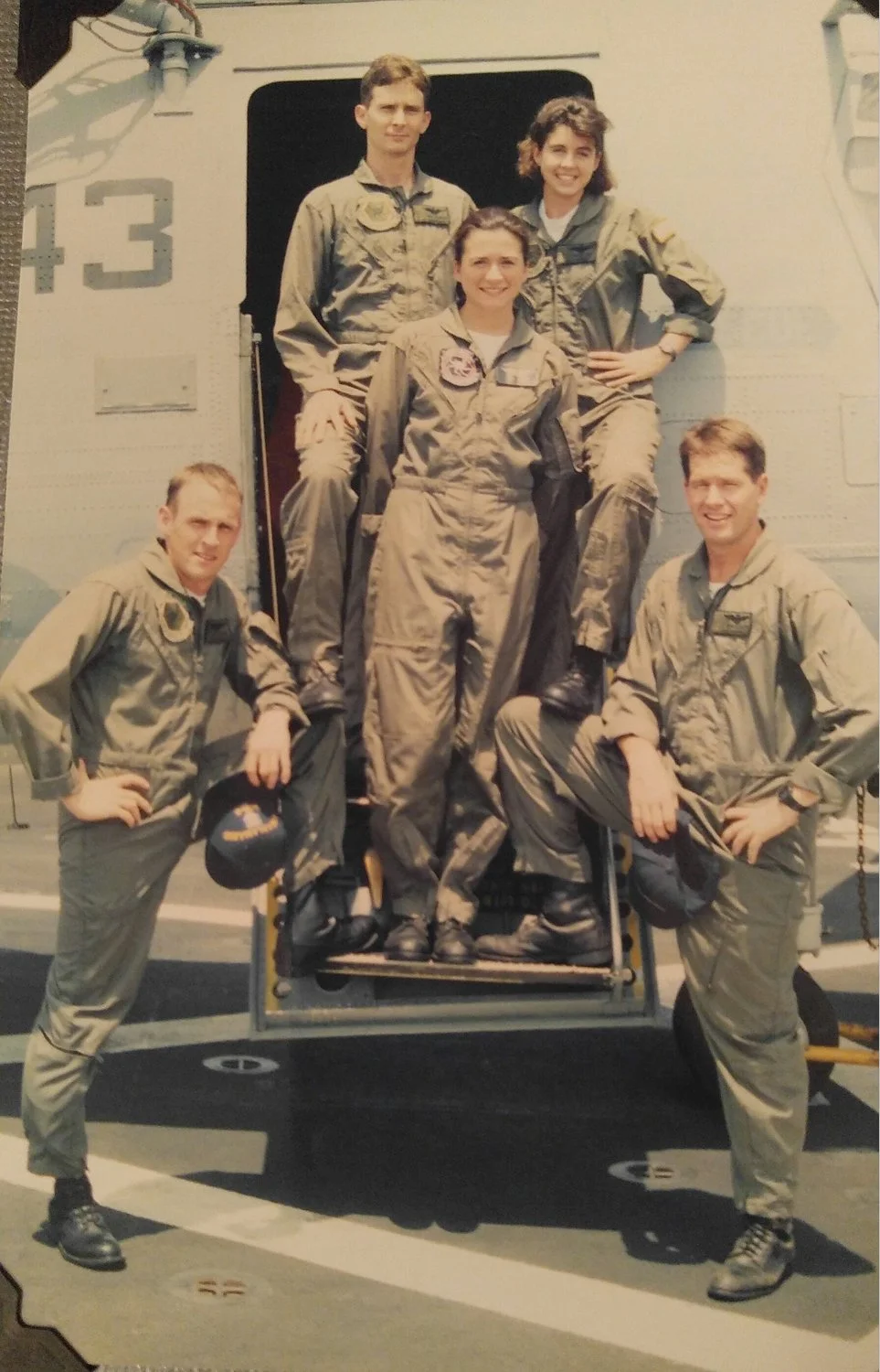 Nancy Lacore and her husband Pat Lacore in flight suits, standing with their Navy flight crew in front of a military aircraft during their years of service.