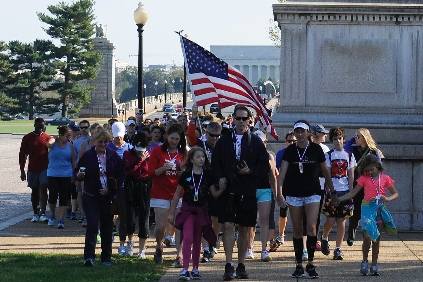 Group of people participating in a patriotic walk near the Lincoln Memorial, with one person holding an American flag.