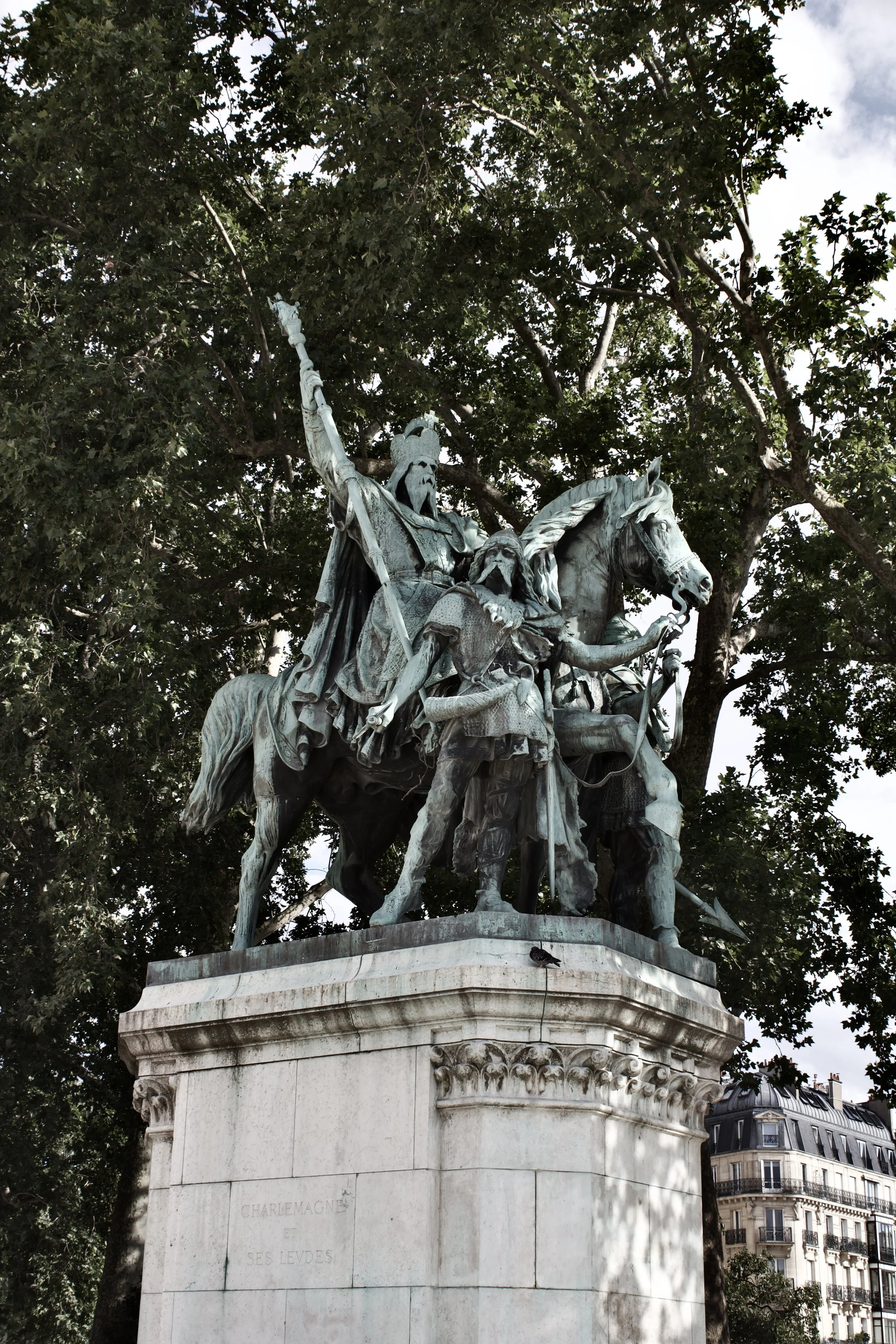Bronze statue of three warriors on horseback with a city building and trees in the background.