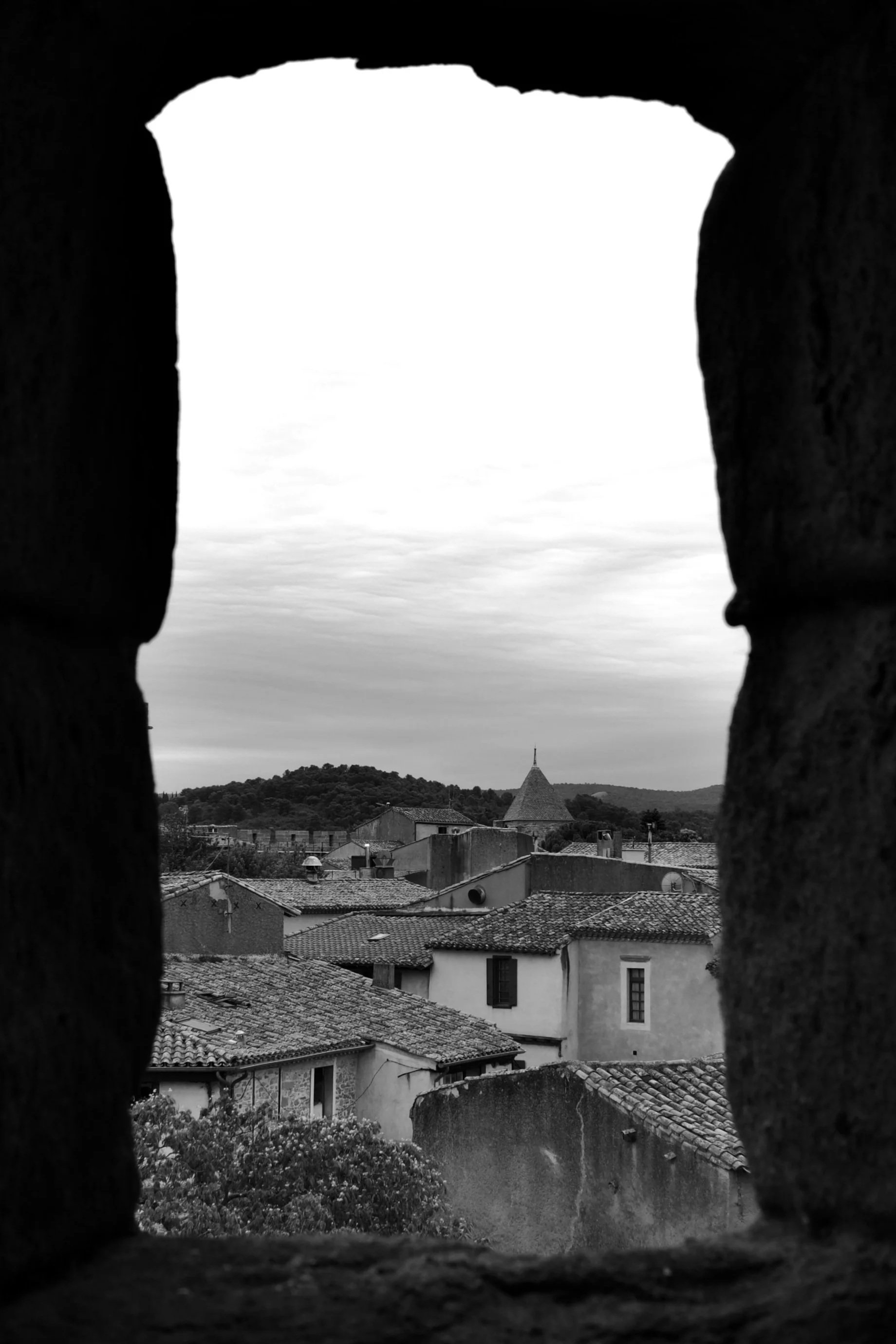 View of a town with tiled rooftops and a church steeple, seen through a small stone window