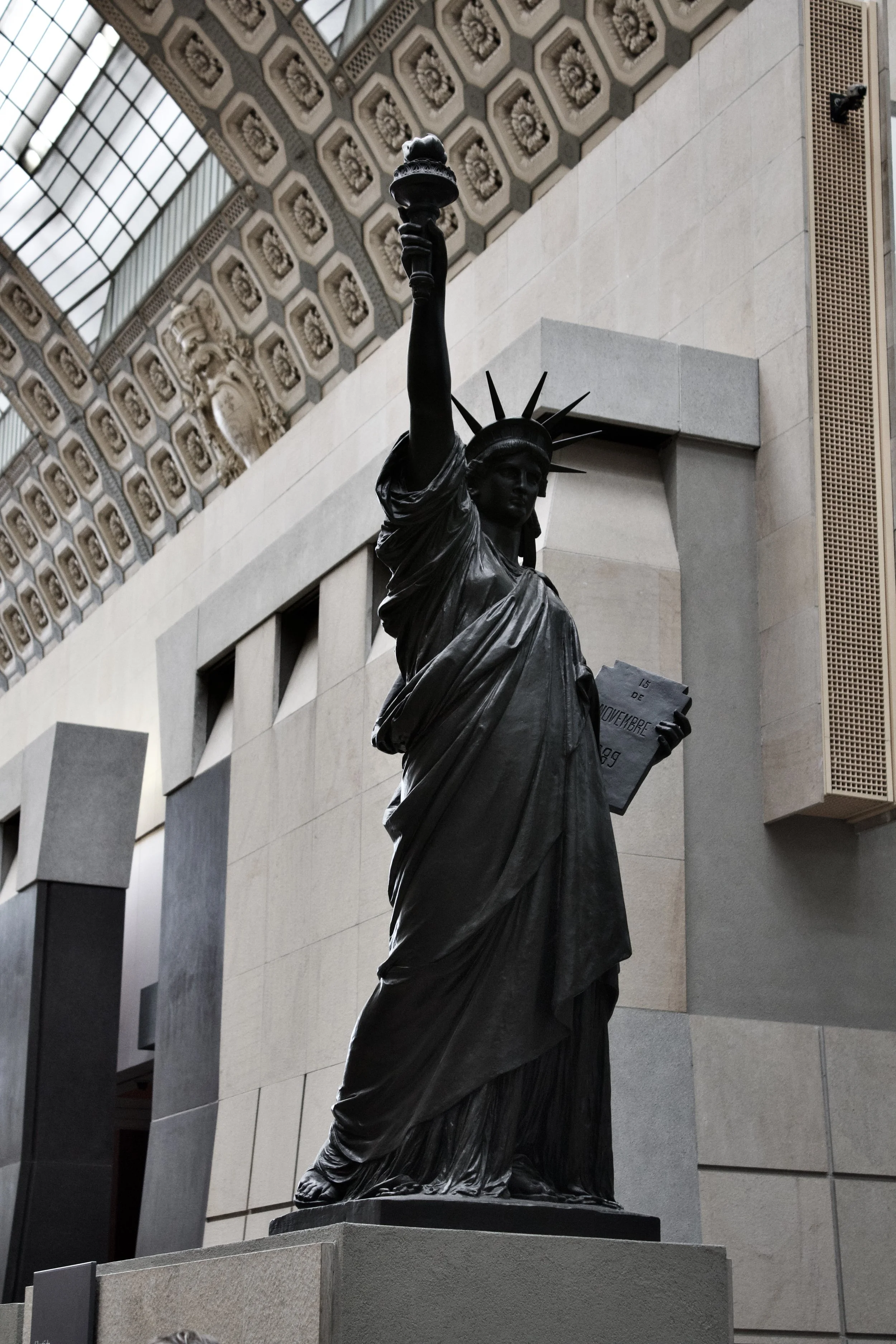 Statue of the Statue of Liberty holding a torch and a tablet, situated indoors with a decorated ceiling and modern architecture.