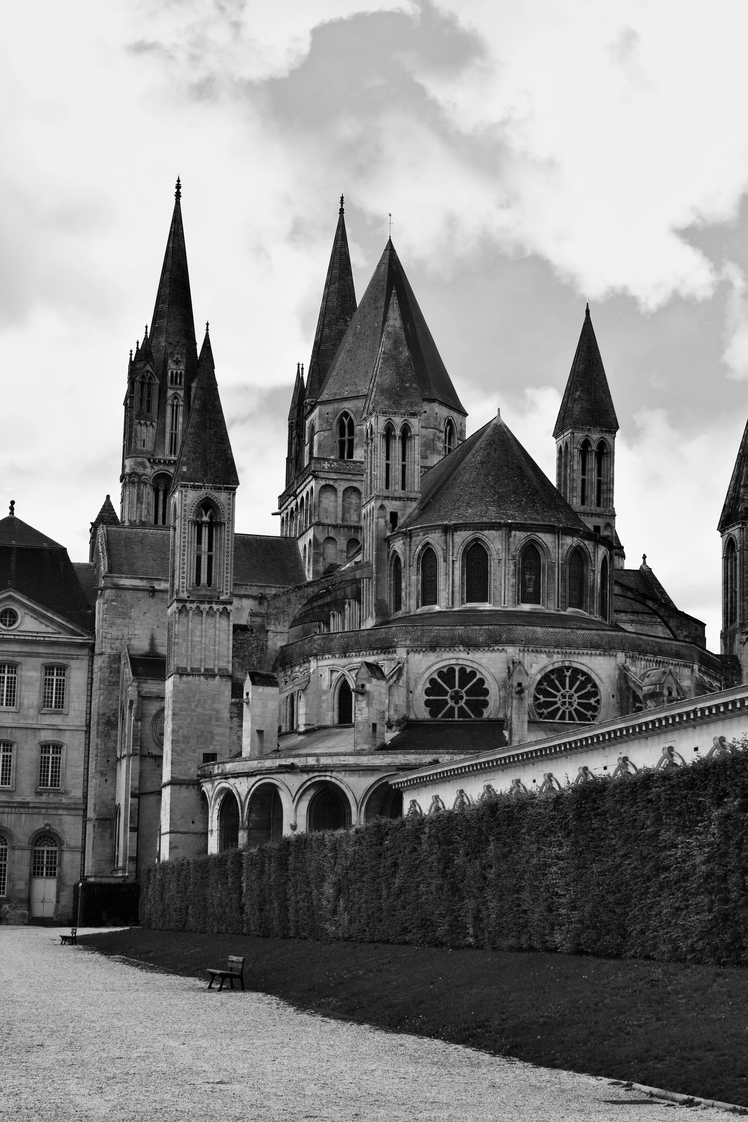 Black and white photo of a historic Gothic-style church with tall spires, stained glass windows, and ornate details, set against a cloudy sky.