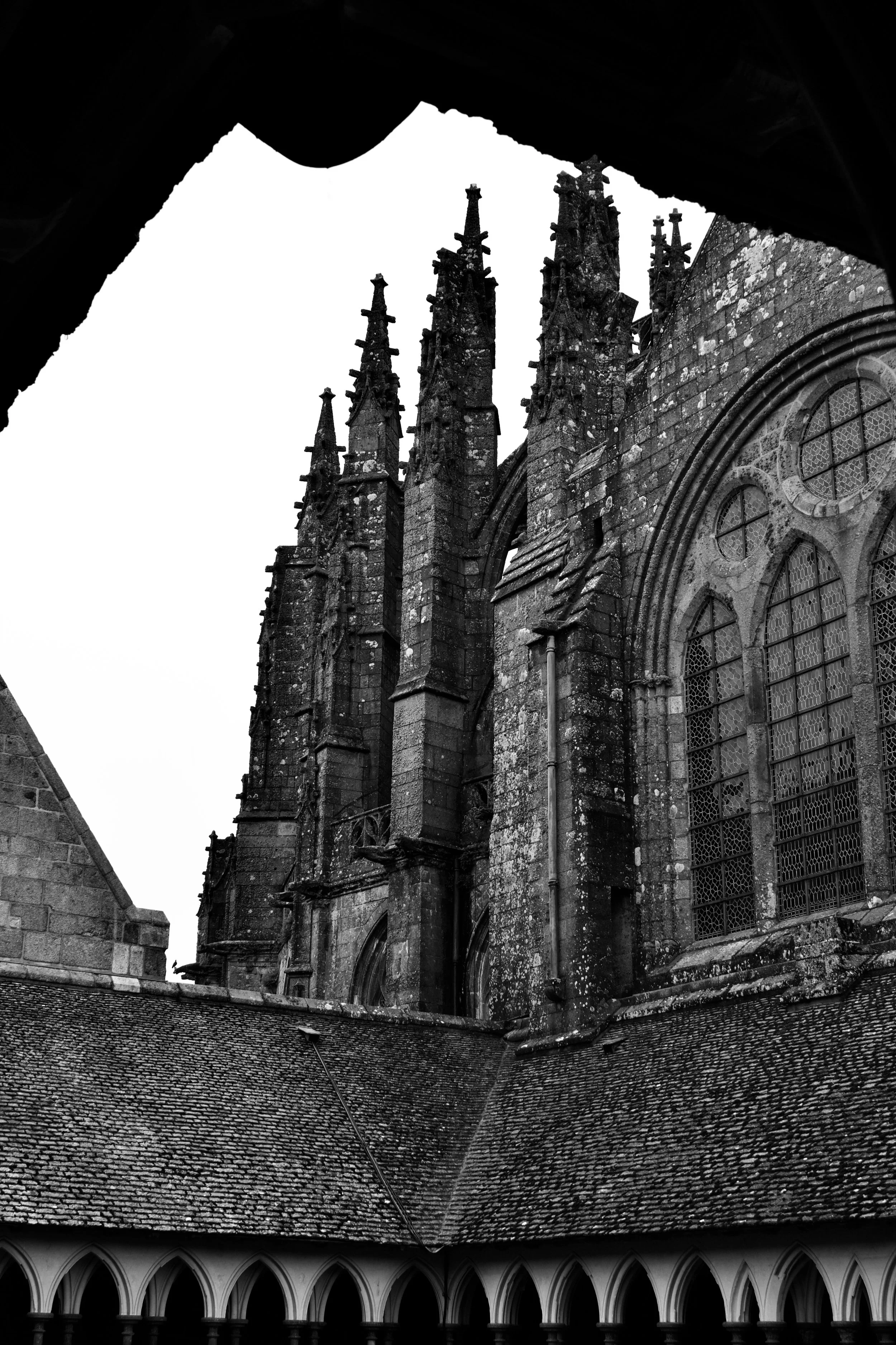 Black and white photo of an old Gothic cathedral viewed from a small window with pointed arches, showing intricate stonework and tall spires.