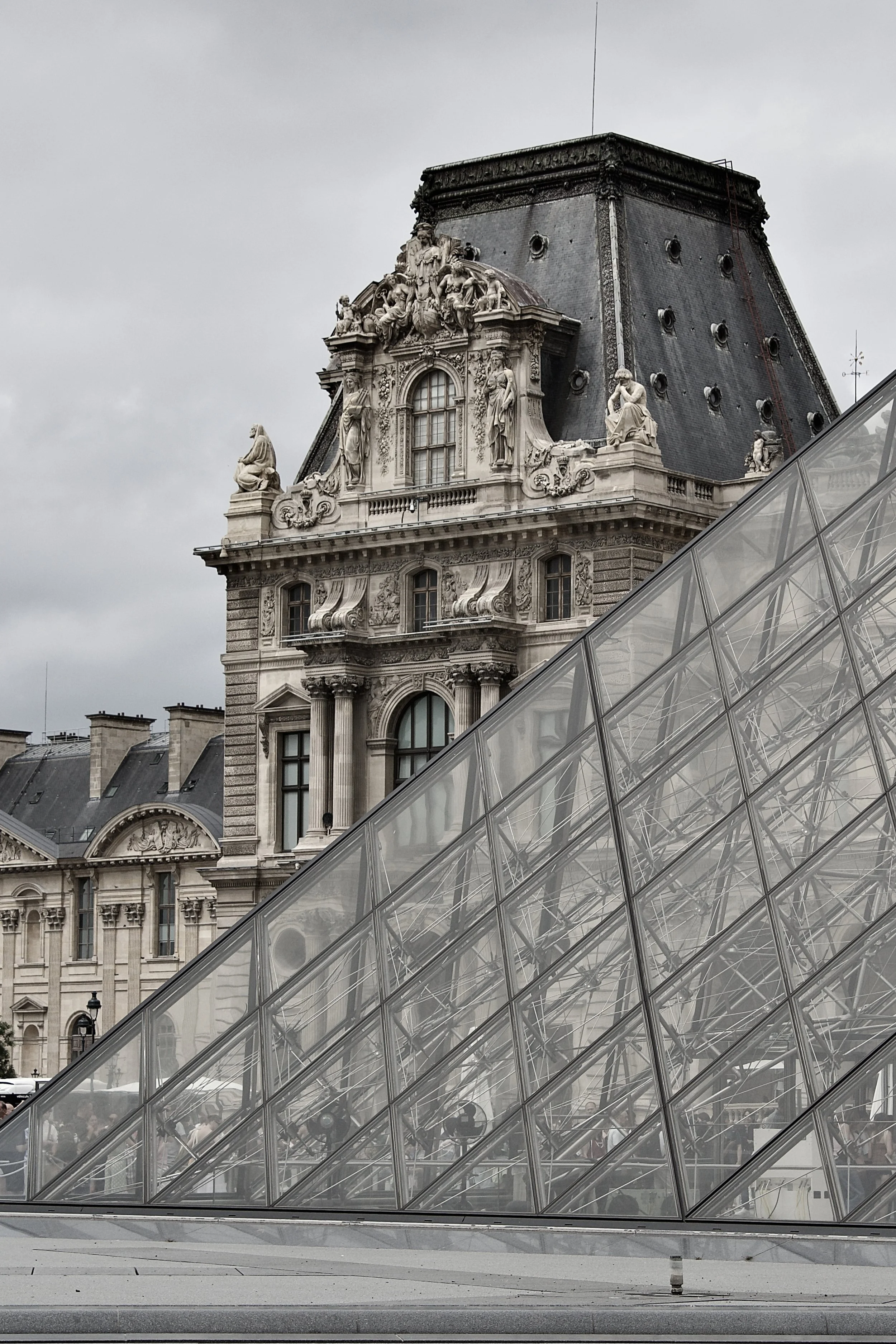 View of historic European building with ornate sculptures on roof and a modern glass pyramid structure in the foreground.