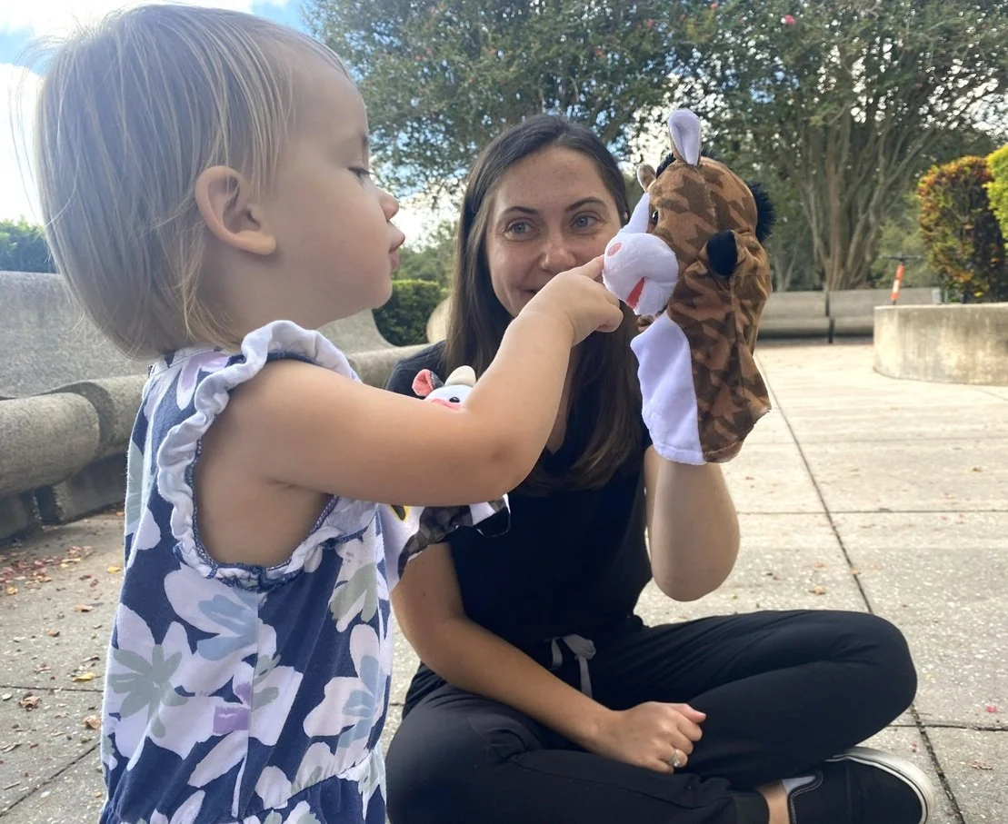 A photograph of a speech language pathologist and a toddler playing with puppets.