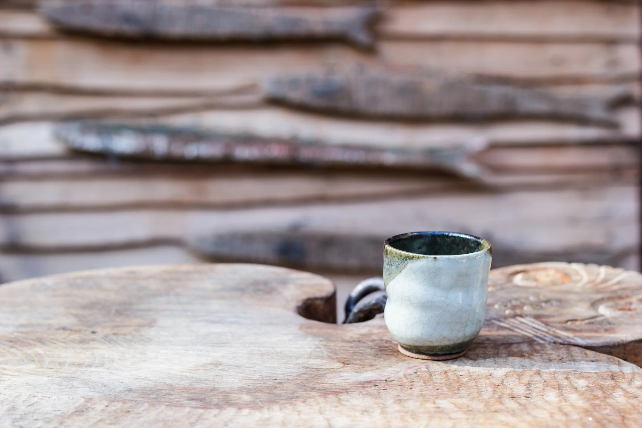 A ceramic mug with a white and black glaze design sitting on a weathered wooden surface with a stack of wooden planks in the background.