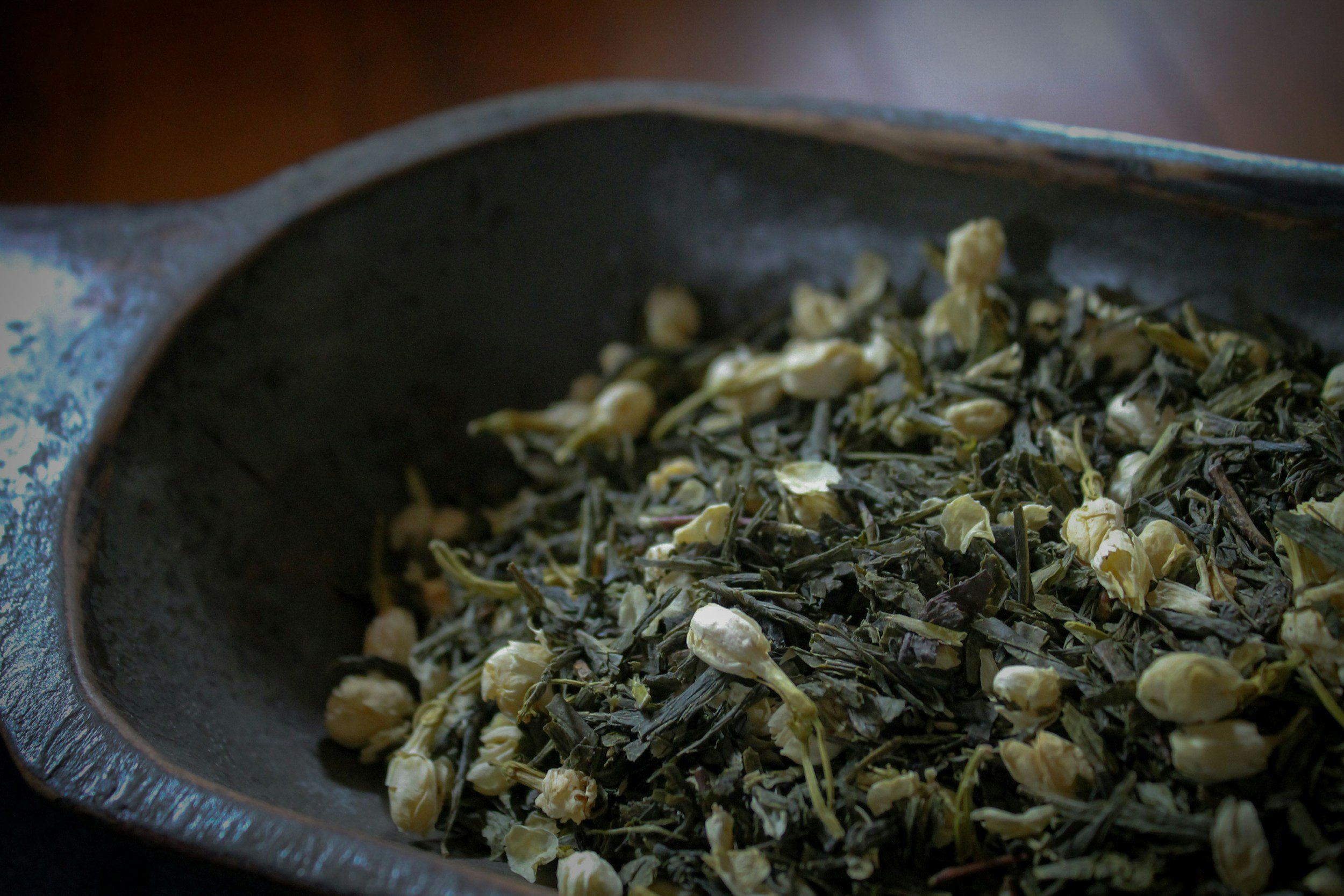 Close-up of dried tea leaves and jasmine flowers in a black bowl.