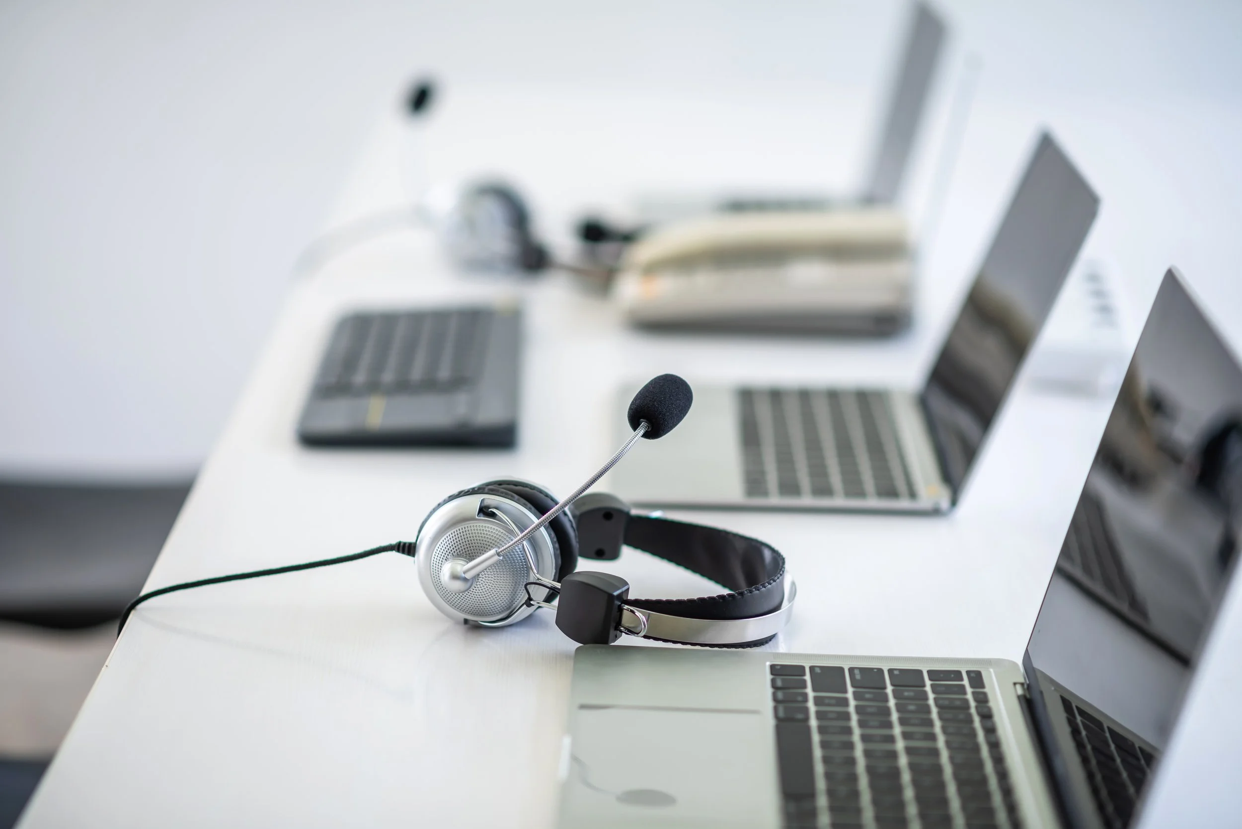 Office desk with three open laptops, a headset with a microphone, and a landline phone.