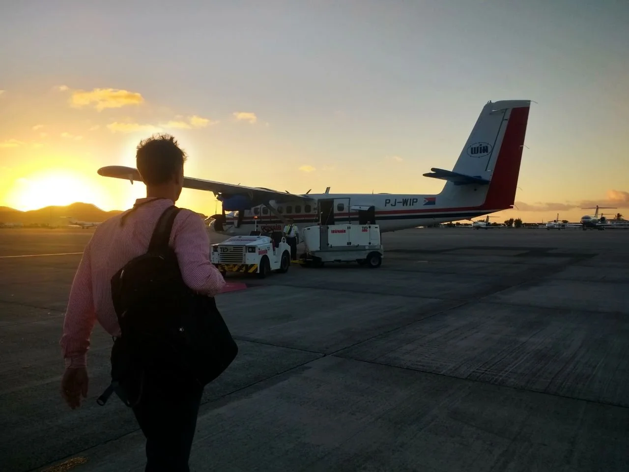 Une personne avec un sac à l'épaule qui marche vers un avion à l'aéroport au coucher du soleil.