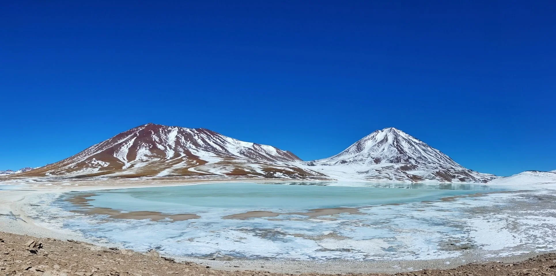 Montagnes enneigées avec un lac gelé au premier plan, sous un ciel bleu clair.