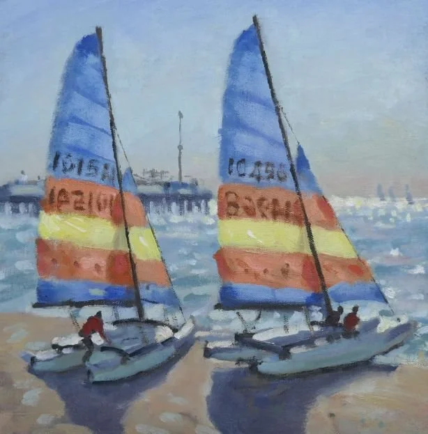 Two sailboats with colorful sails are docked near a pier on a calm body of water with a city skyline in the background.