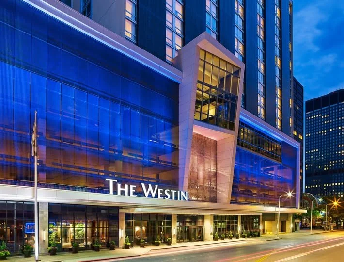 The exterior of The Westin hotel building at dusk with modern glass architecture and illuminated signage.