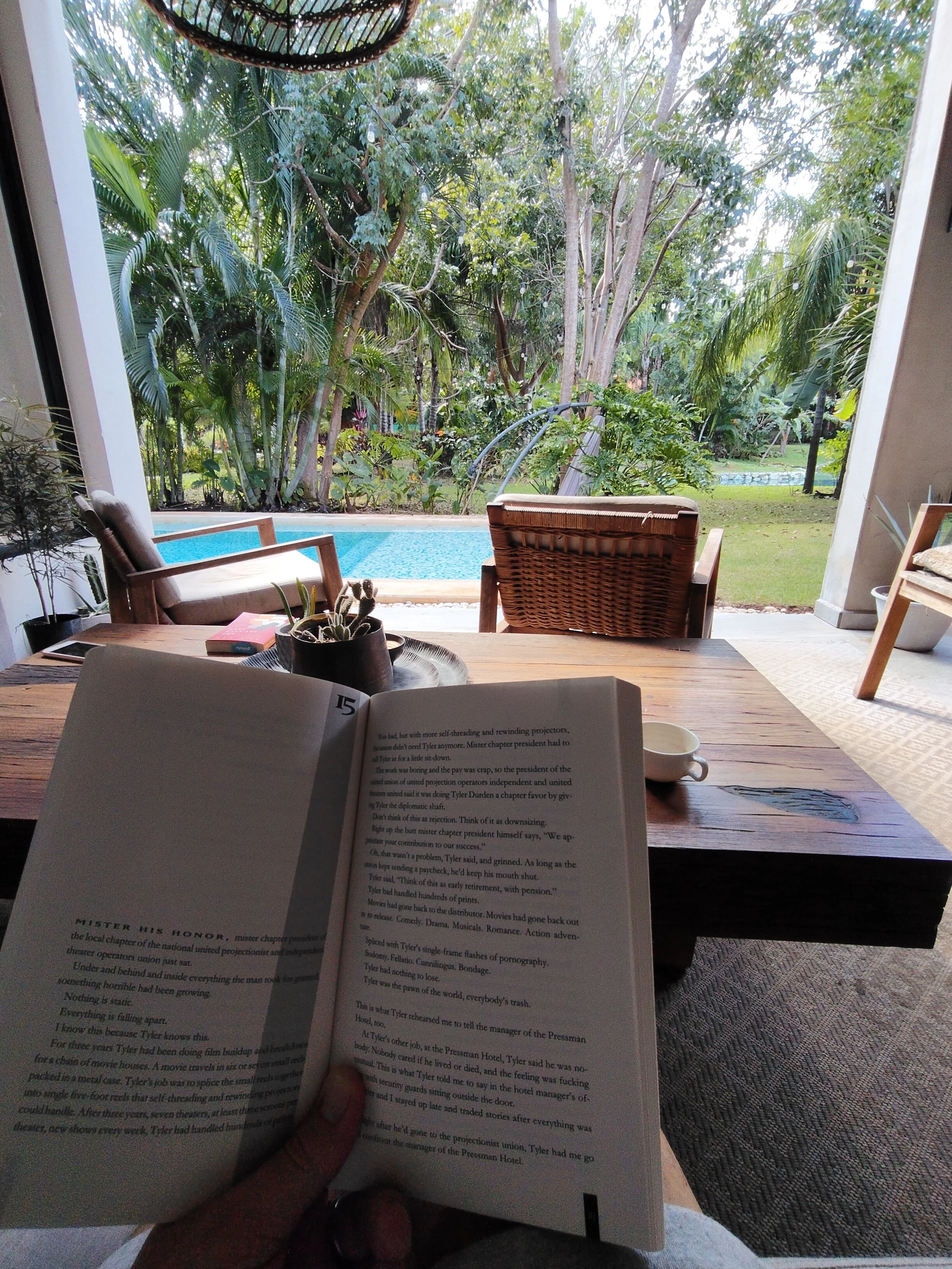Someone reading a book overlooking a pool and tropical plants