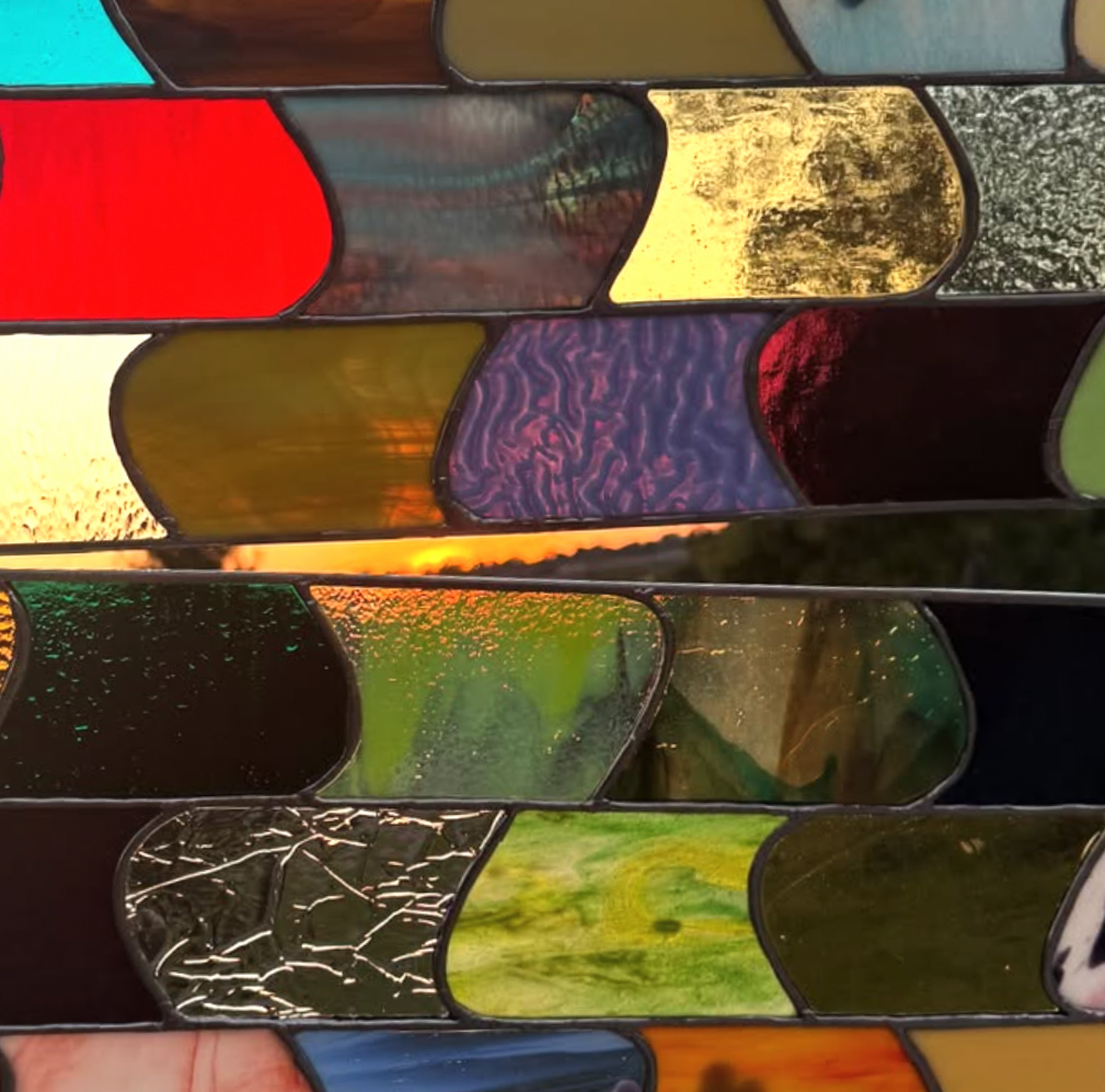Close-up of stained glass window with various colorful glass pieces, reflecting natural scenes and abstract patterns.