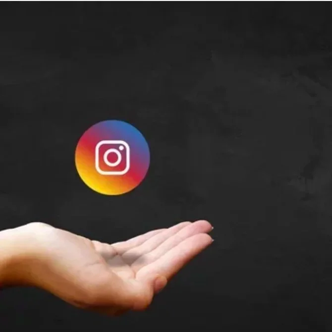 A person's hand with the palm facing up, appearing to support or hold a floating colored Instagram logo against a black background.