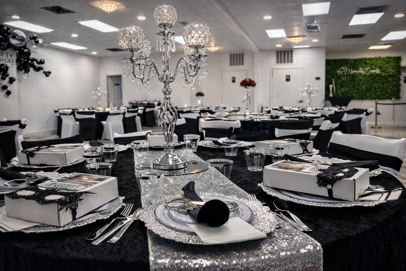 Elegant banquet table set for a celebration with black and white decorations, silver accents, and a candelabra centerpiece in a decorated event hall.
