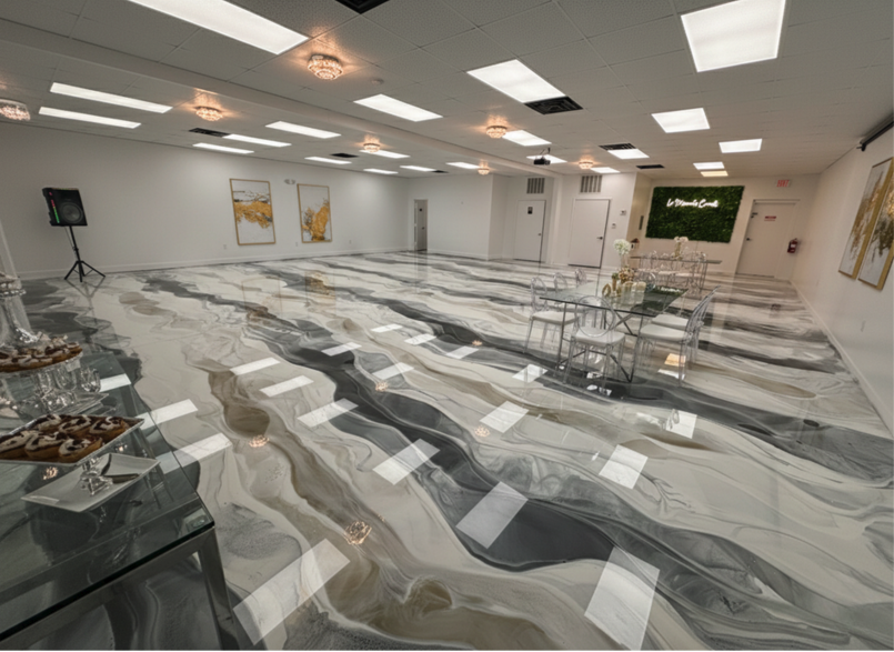 Empty event or conference room with marble flooring, ceiling lights, and seating area with glass tables and transparent chairs, decorated with artwork on white walls and a green wall with writing.