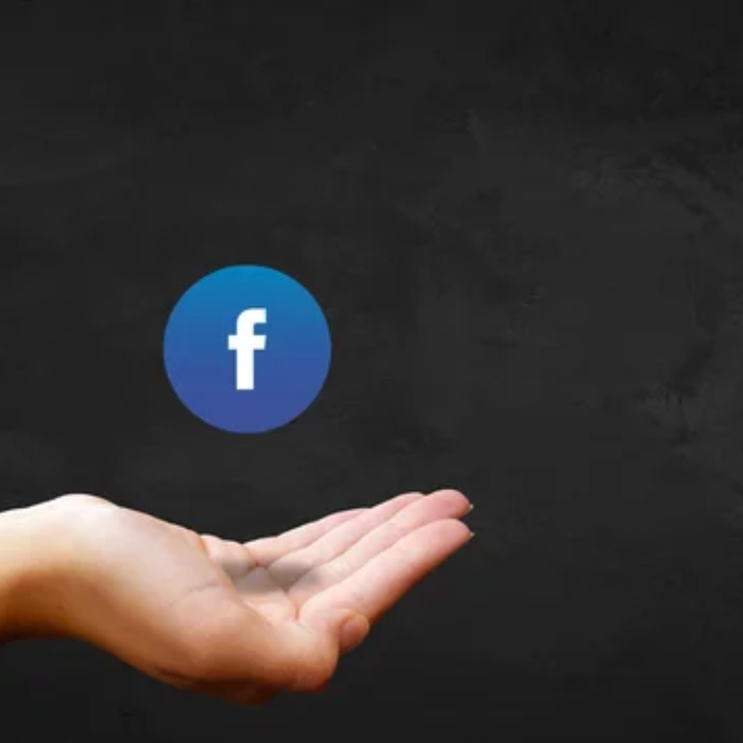 A hand is positioned with the palm facing up below a blue Facebook logo floating in the air against a dark background.