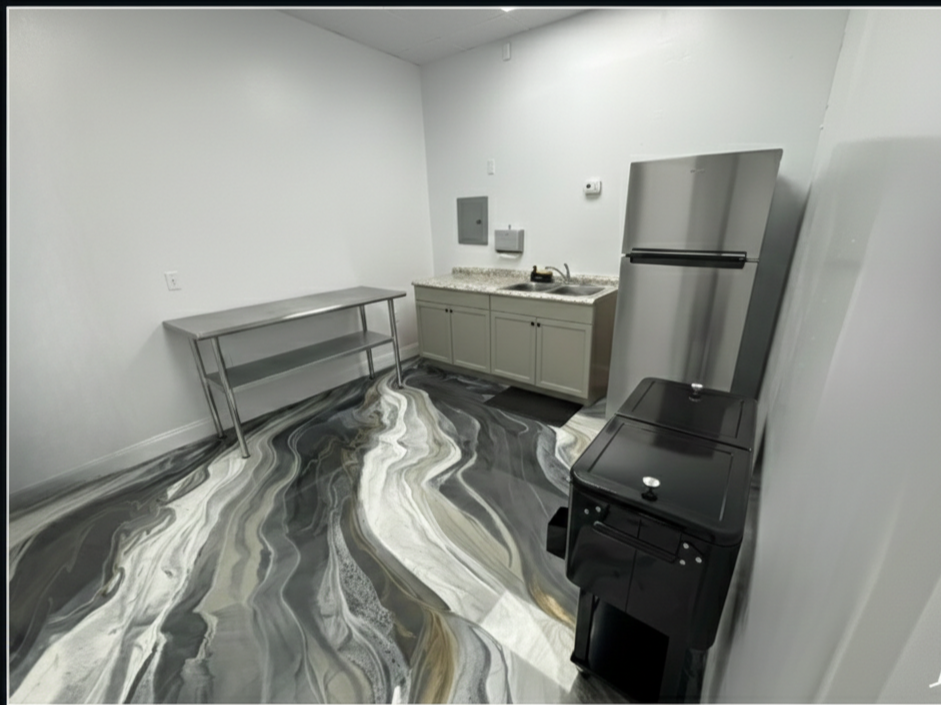 Empty kitchen with stainless steel refrigerator, black stove, gray cabinets, granite countertop, stainless steel table, and a marble-patterned floor.