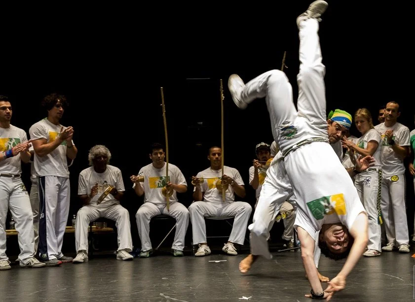 People dressed in white performing capoeira with one person doing a handstand.