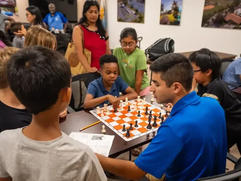 Group of children and an adult playing chess at a table in a busy indoor setting.