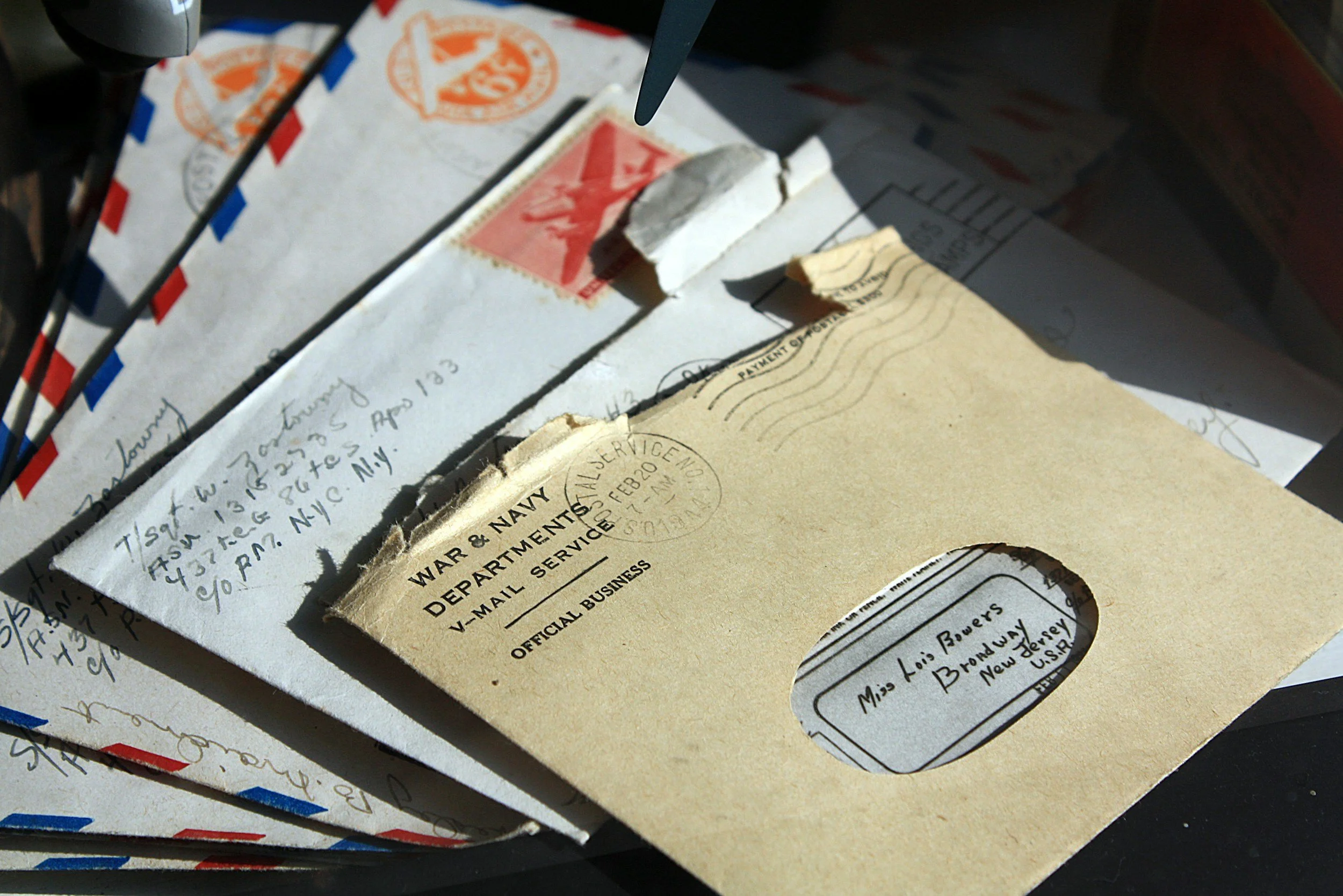 Stack of vintage military envelopes, with one addressed to Miss Lois Bowers in New Jersey, and an airmail envelope from the War & Navy Department, with visible postal stamps and handwritten addresses.