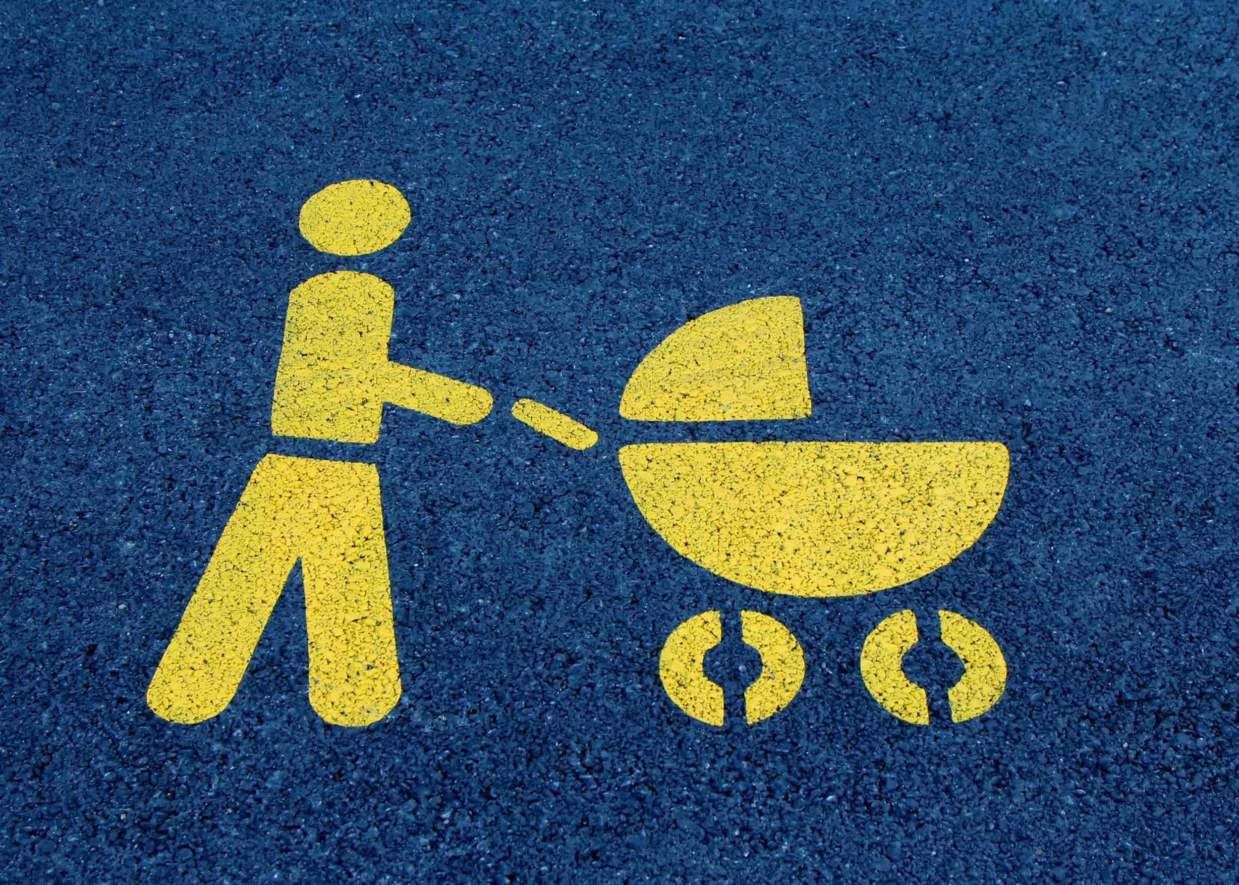 Yellow painted symbol of a person pushing a baby stroller on a blue pavement.