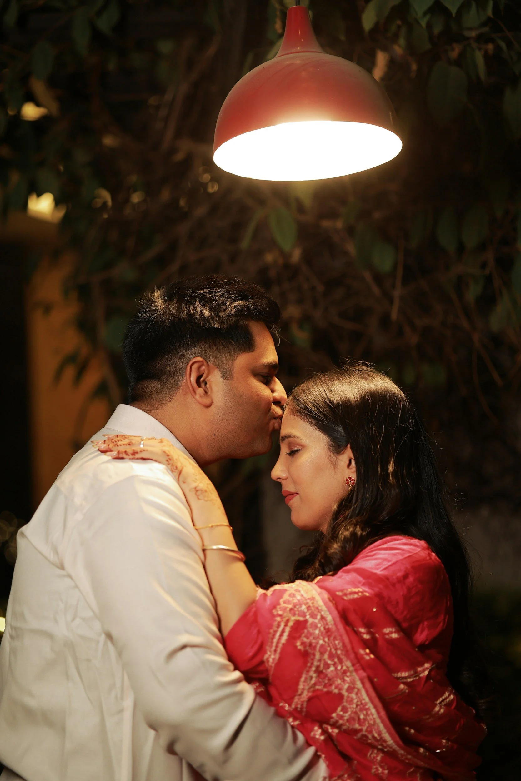 A man and woman share an intimate moment in a warmly lit setting, with the man gently kissing the woman's forehead.