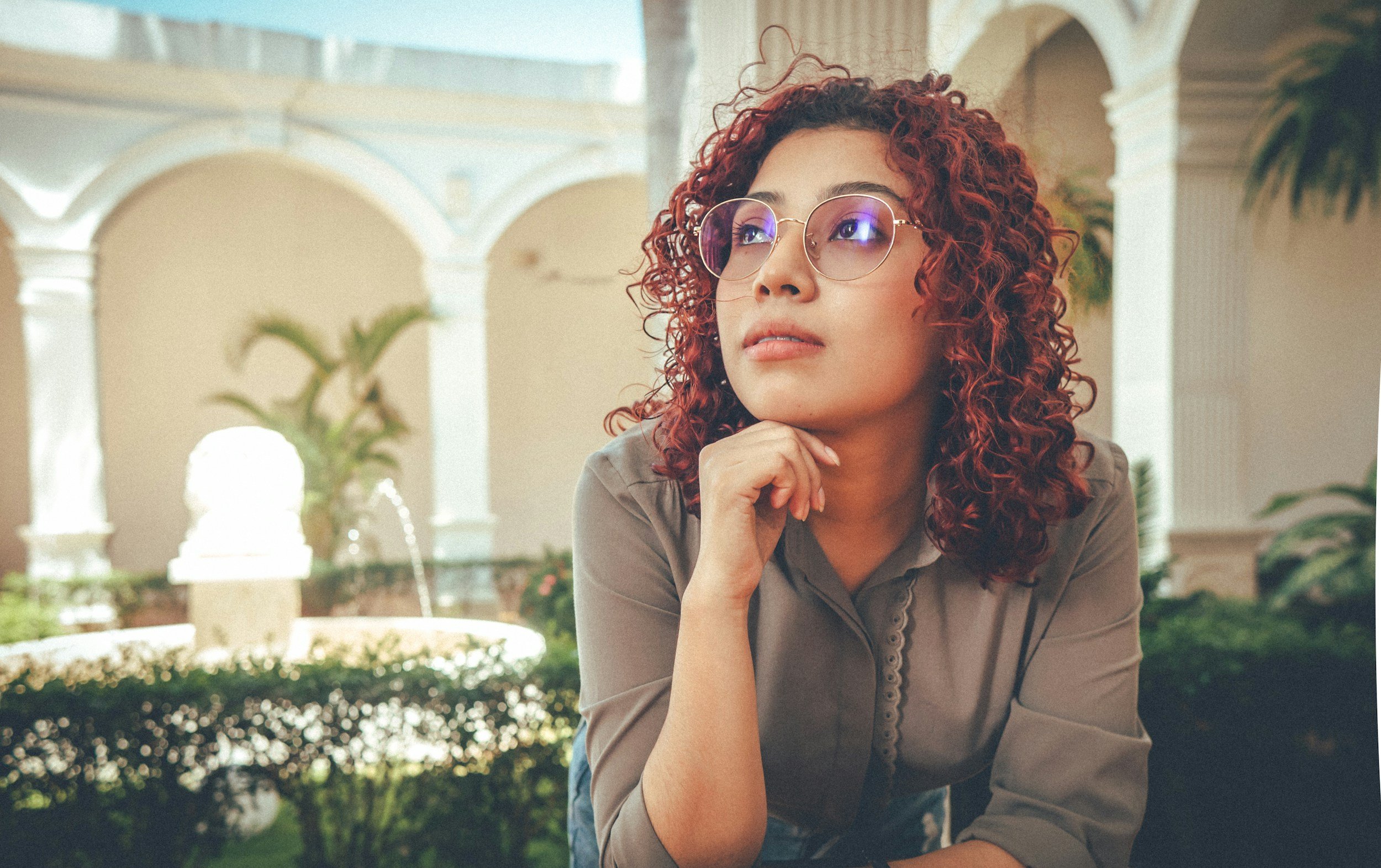 Woman with tan skin, curly maroon hair, and eyeglasses thinking about questions about adoption. Woman considering confidential appointment with Starr Adoption Services to discuss her adoption choices of arizona. Making an adoption plan is an option.