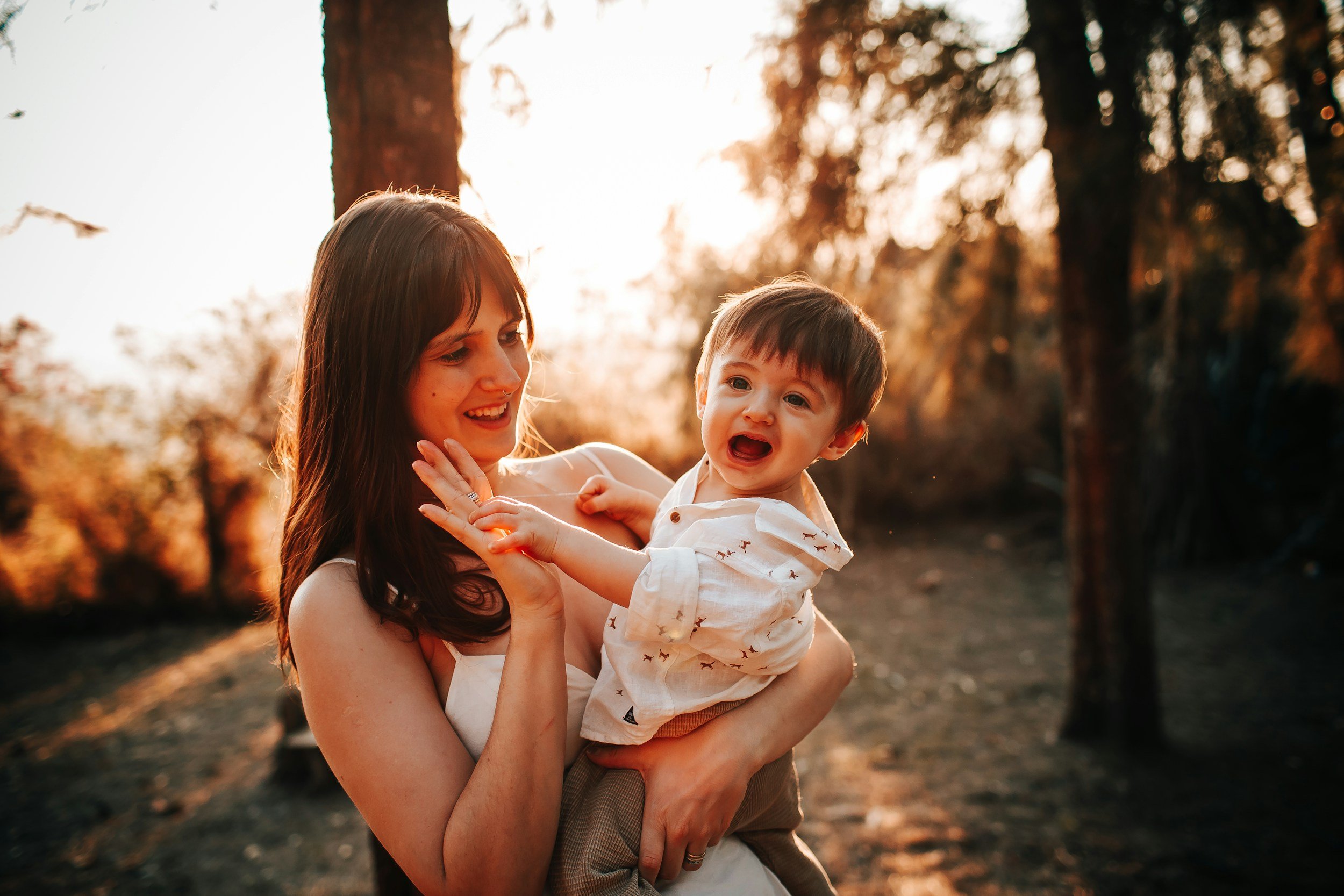 A woman holding a young boy outdoors during sunset, with trees and warm sunlight in the background considering adoption for her child and learning how to get pregnant help options to create an adoption plan.
