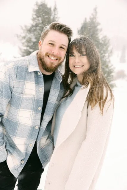 A smiling man and woman standing close together outdoors in a snowy environment.