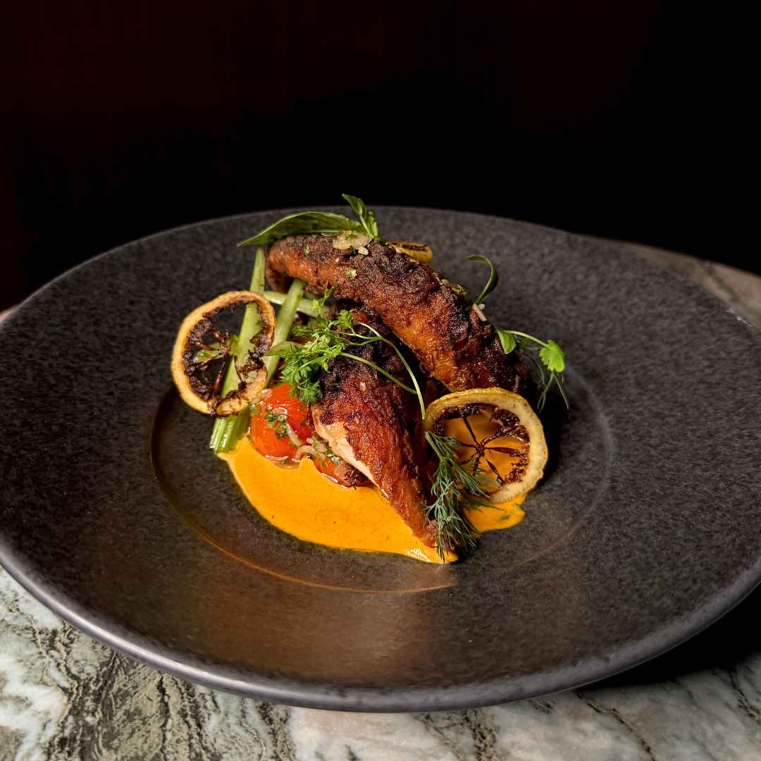 Grilled fish with lemon slices, herbs, and sauce on a black plate.
