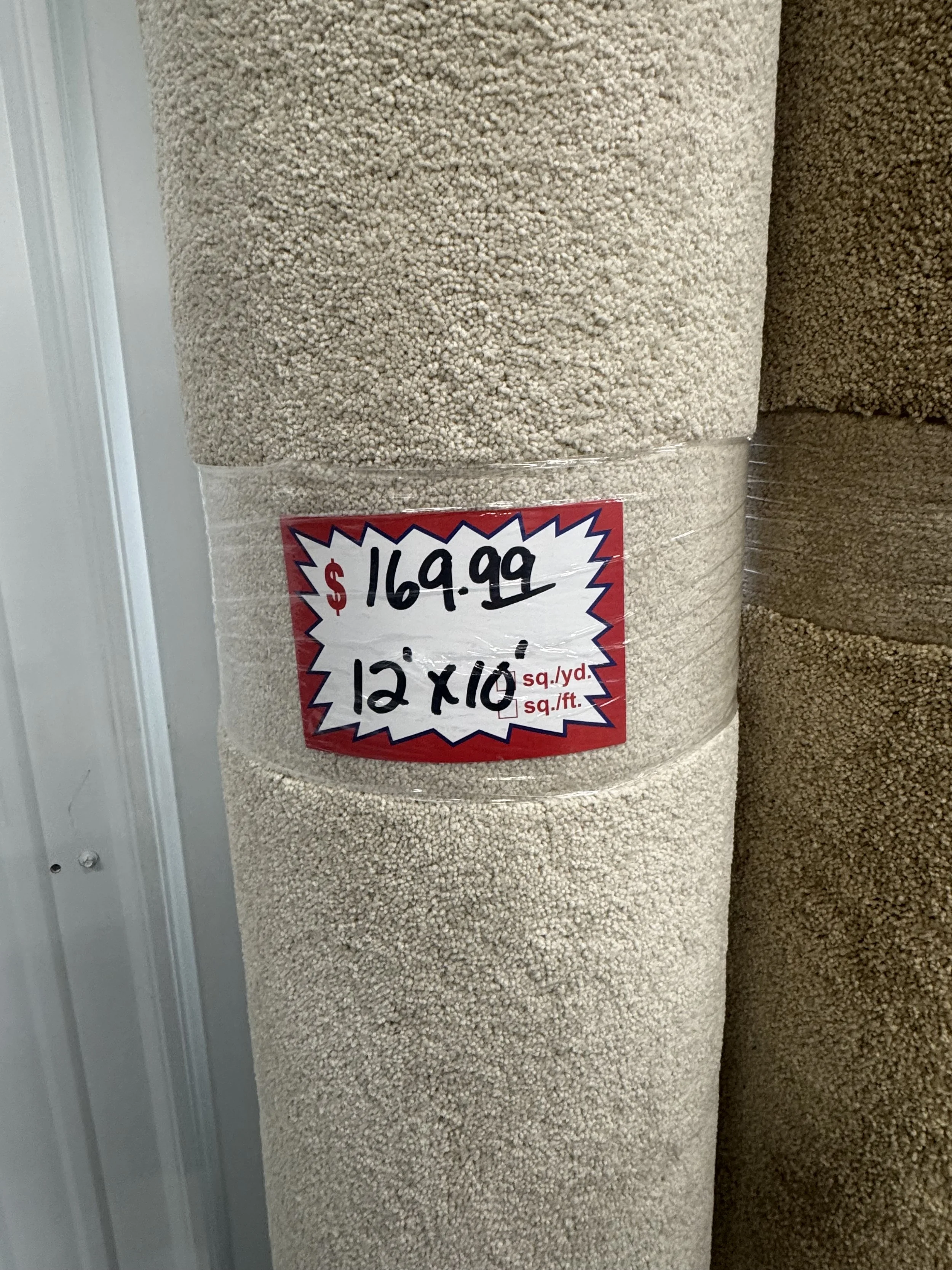 A roll of beige carpet with a price tag indicating 169.99 dollars, measuring 12 feet by 10 feet.
