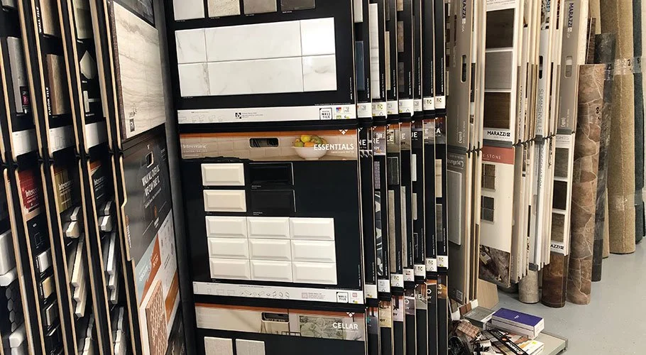Display of various tile samples in a home improvement store, with samples on racks and a digital screen showing tile options.